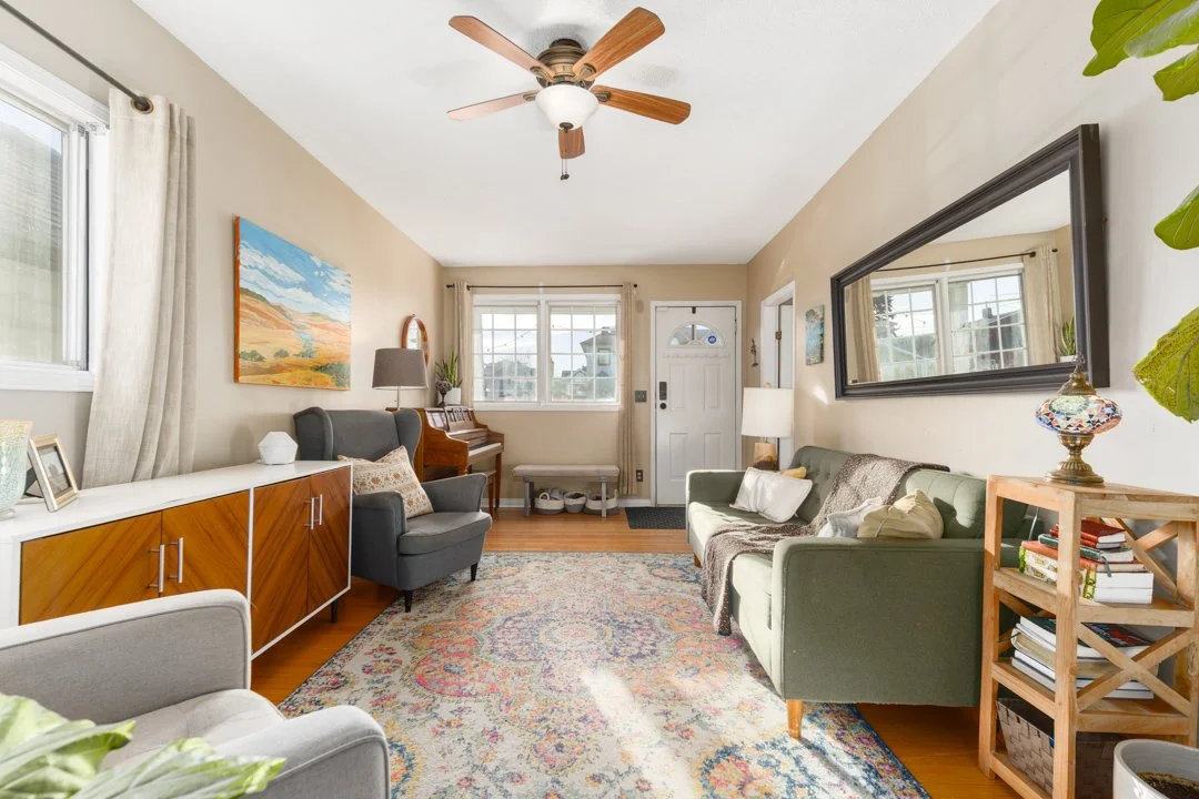 Living room with beige walls, white ceiling, ceiling fan, hardwood floor, sofa, armchair, coffee table, bookshelves, large mirror, and windows