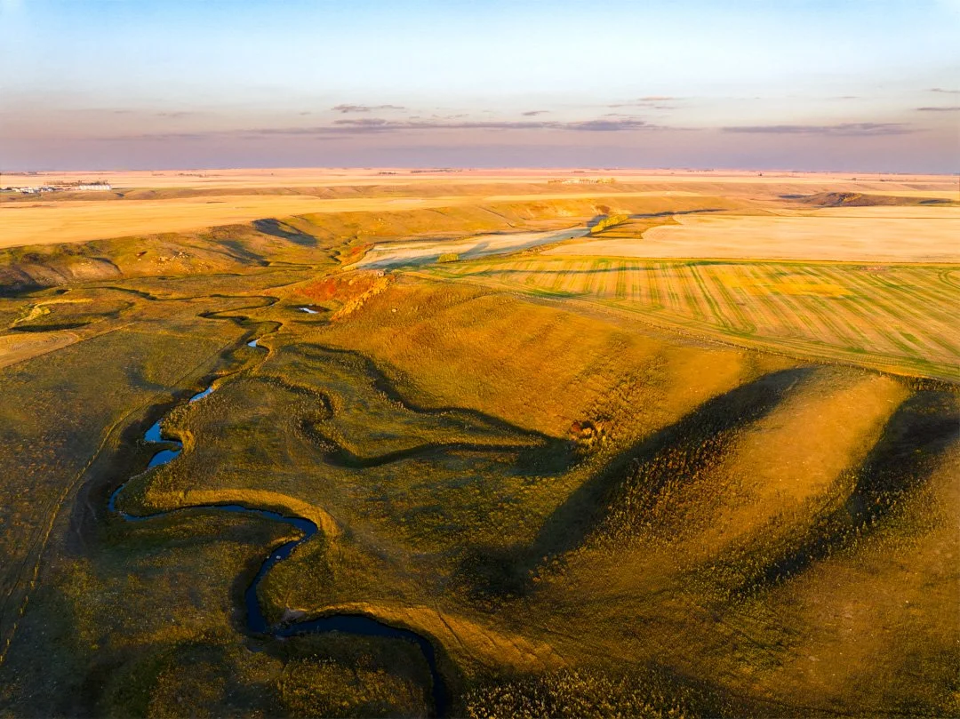 Aerial view of rolling hills and a winding river through a rural landscape during sunset.