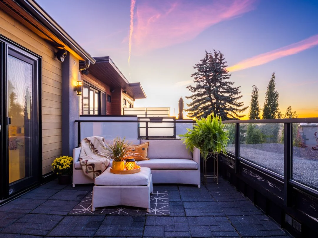 Balcony with outdoor furniture, plants, and a sunset sky.