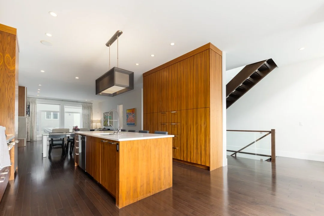 Modern kitchen with wooden cabinets and island, dark hardwood floors, and an open living area in the background
