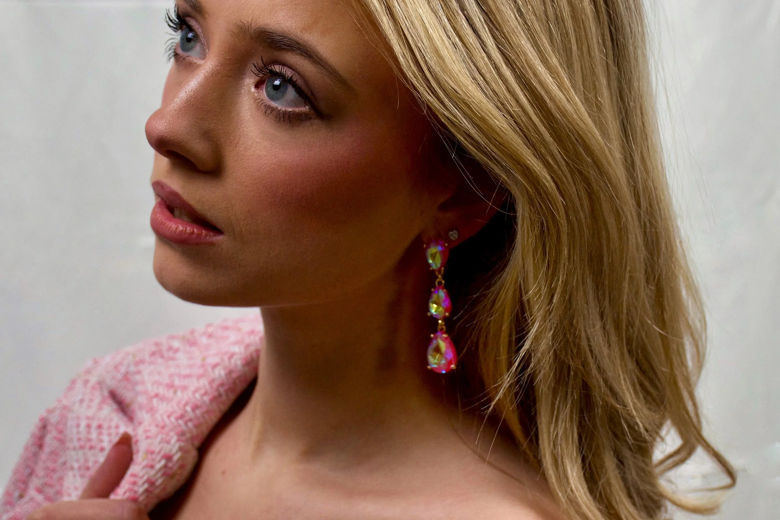 Close-up of a woman with blonde hair and blue eyes wearing a pink dress and colorful earrings.