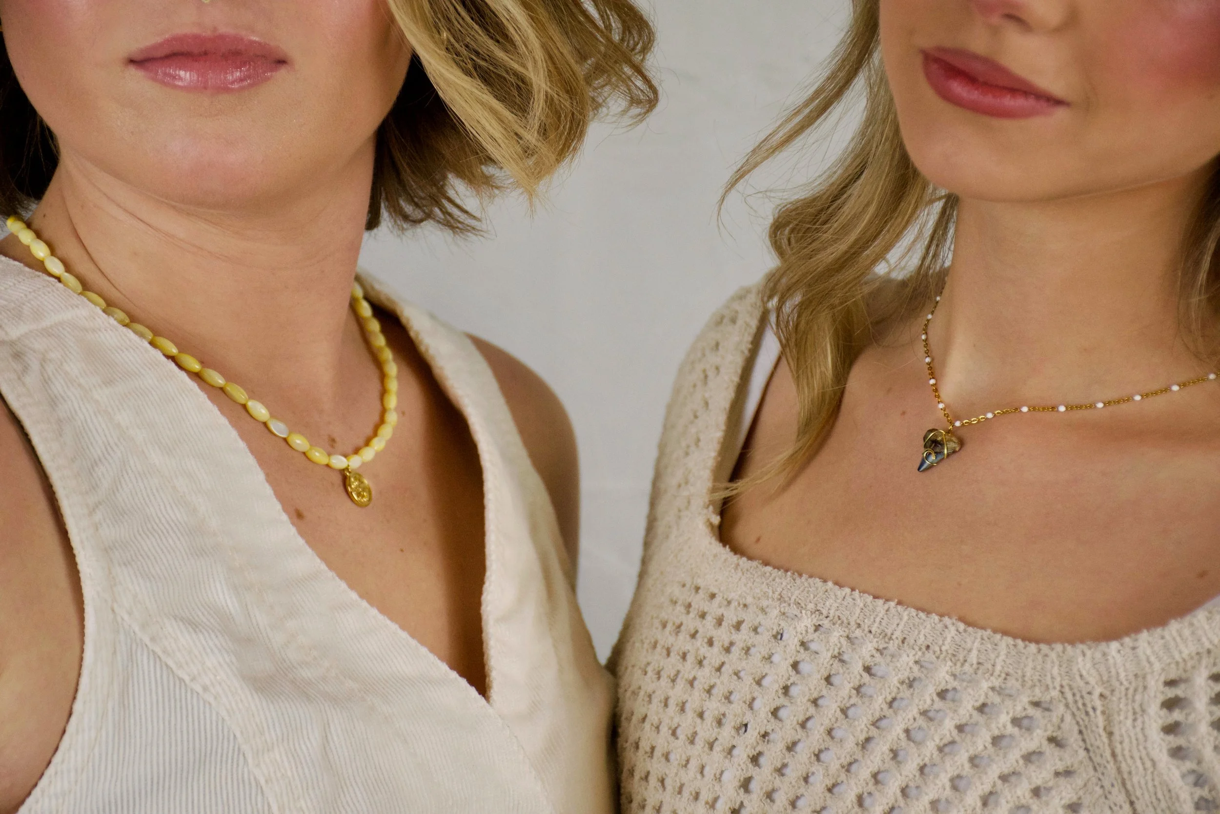 Close-up of two women wearing beige tops and necklaces, with only their lower faces and upper chests visible.