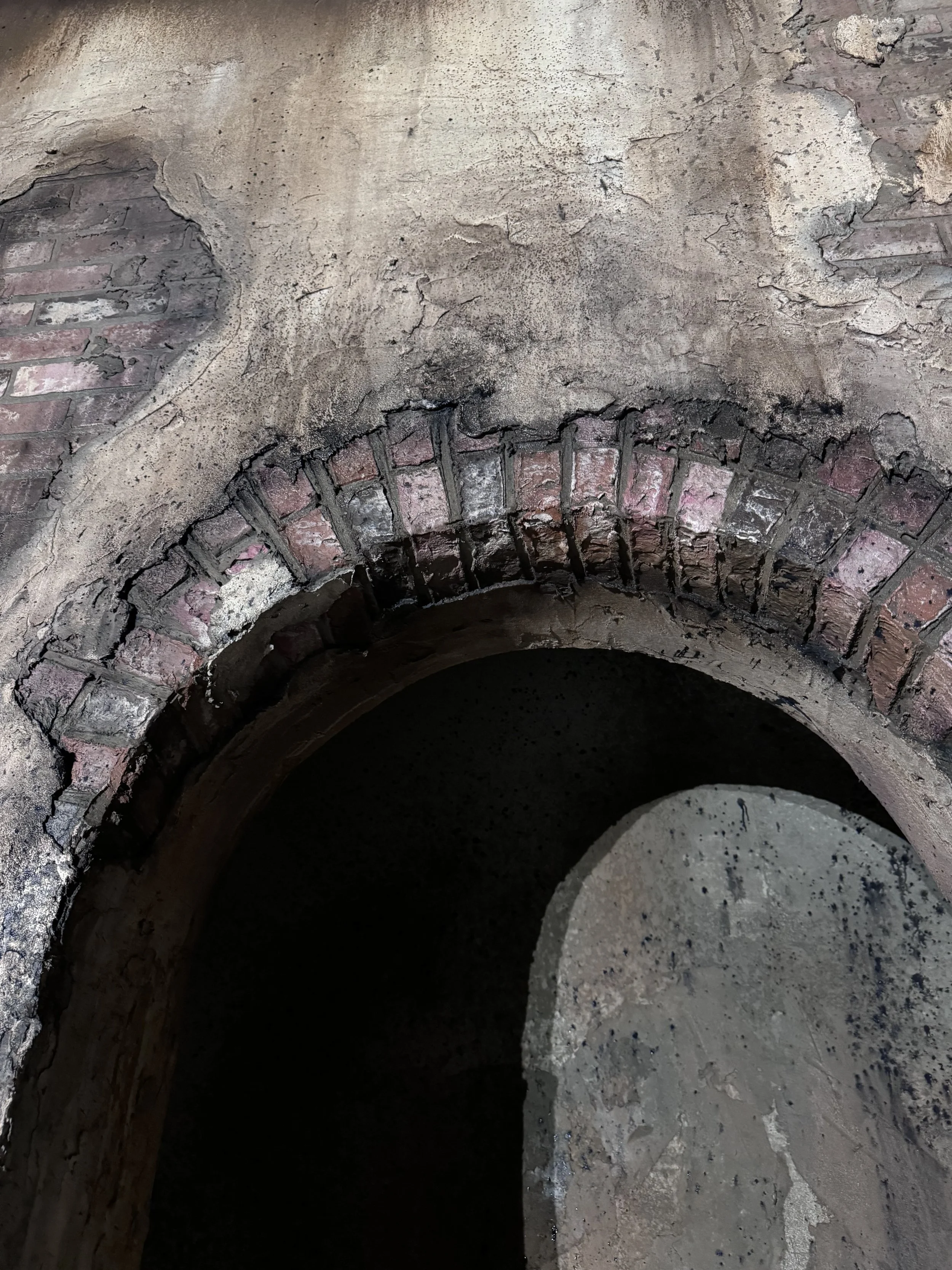 Close-up view of an old, weathered brick archway with peeling plaster on the surrounding wall.