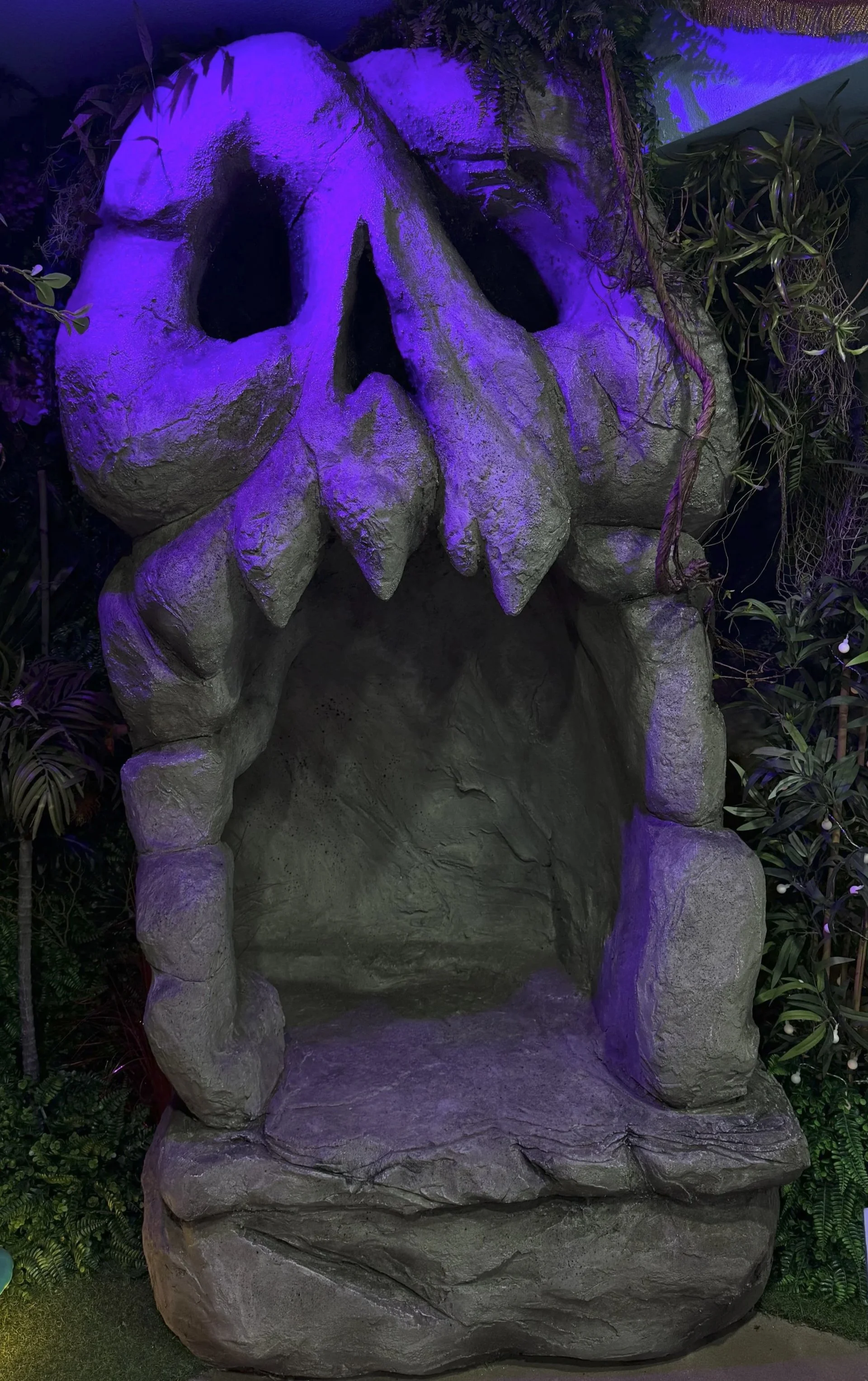 Rock formation designed to look like a large skull with purple lighting, surrounded by plants.