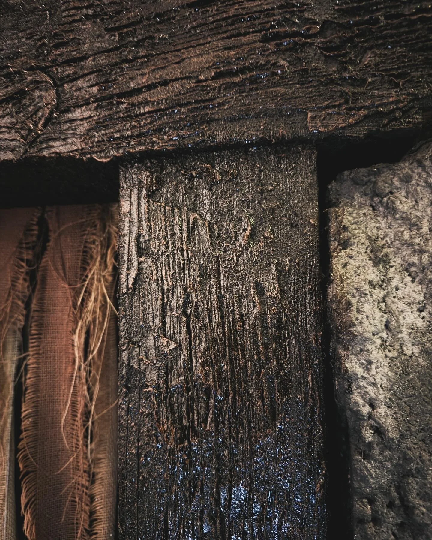 Close-up of weathered, dark, wooden and stone structures, showing textured surfaces and rough details.