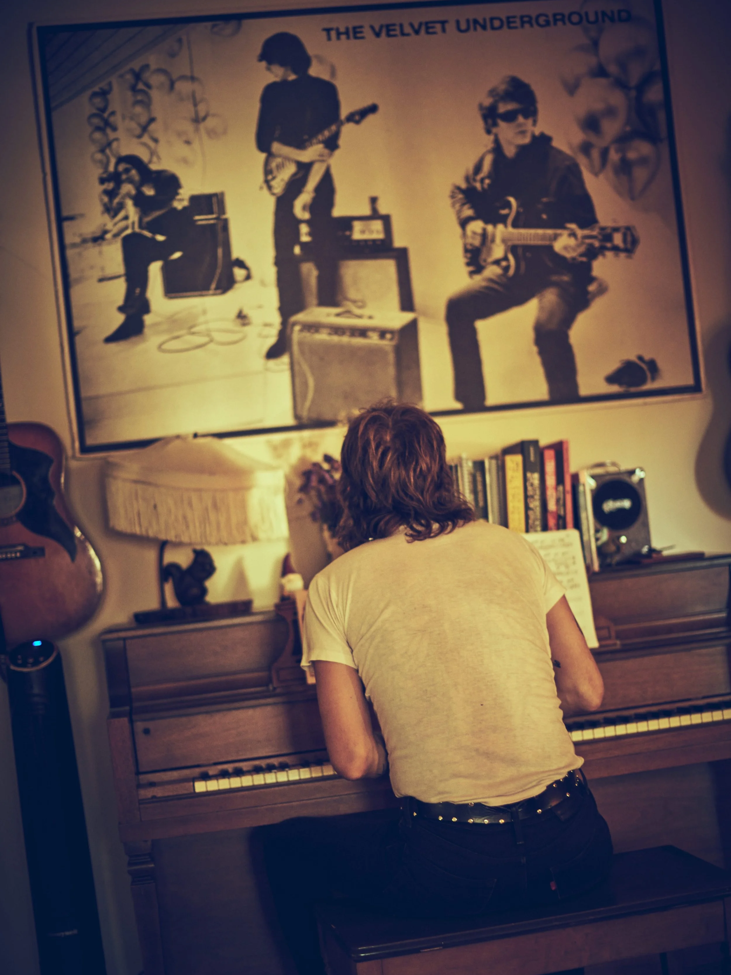 Person playing piano in a room decorated with guitars and a large poster of The Velvet Underground band.
