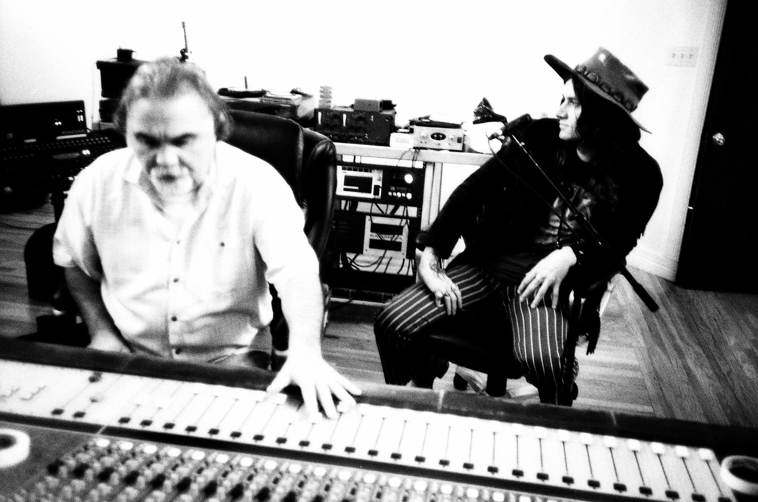 Black and white photo of a man playing a keyboard and a woman sitting with a microphone, wearing a hat with stars, in a recording studio.