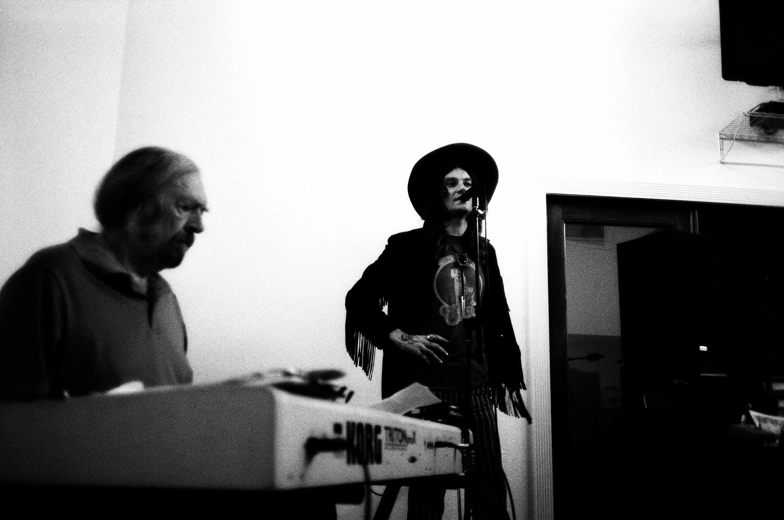 Black and white photo of a woman singing into a microphone with a man playing a keyboard.