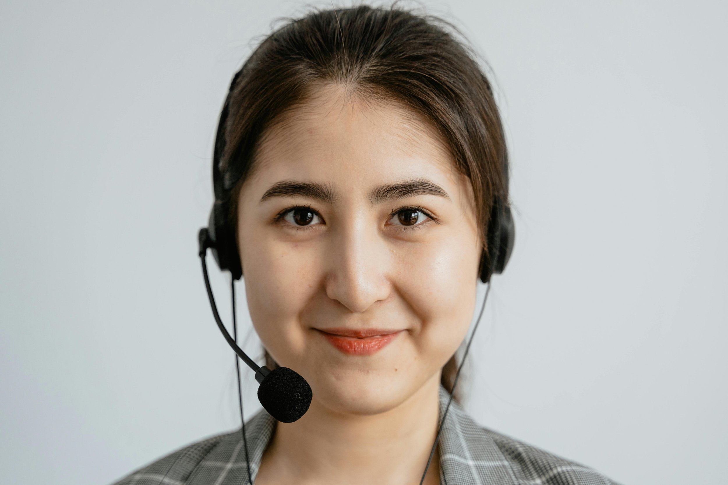 A woman with brown hair wearing a headset with microphone, smiling at the camera.