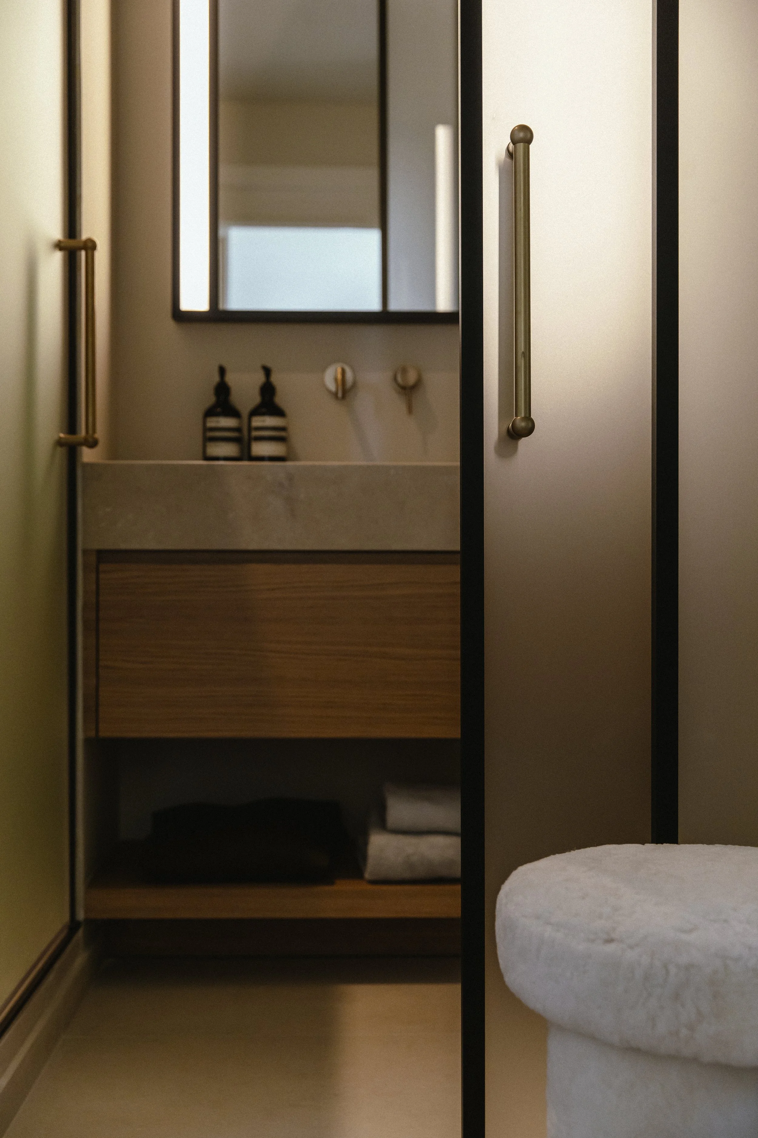 A view through a partially open beige sliding door into a bathroom with a sink, mirror, and toiletries