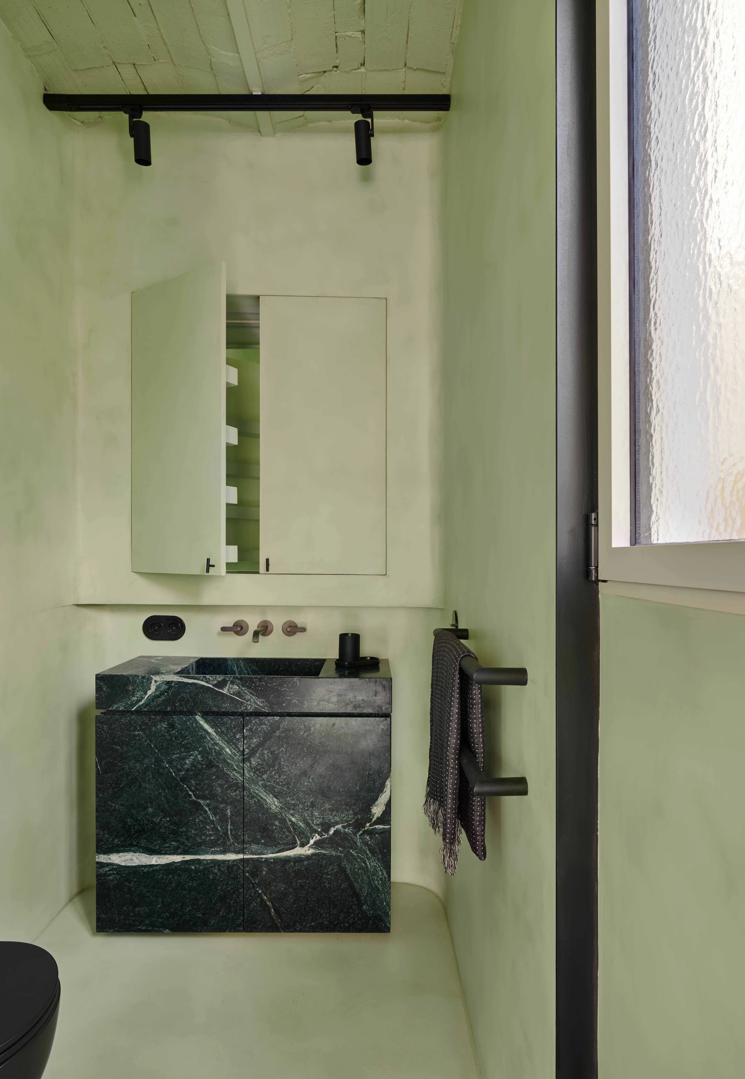 Minimalist bathroom with pale green walls, a black marble sink vanity, and a large window with a view of a body of water.