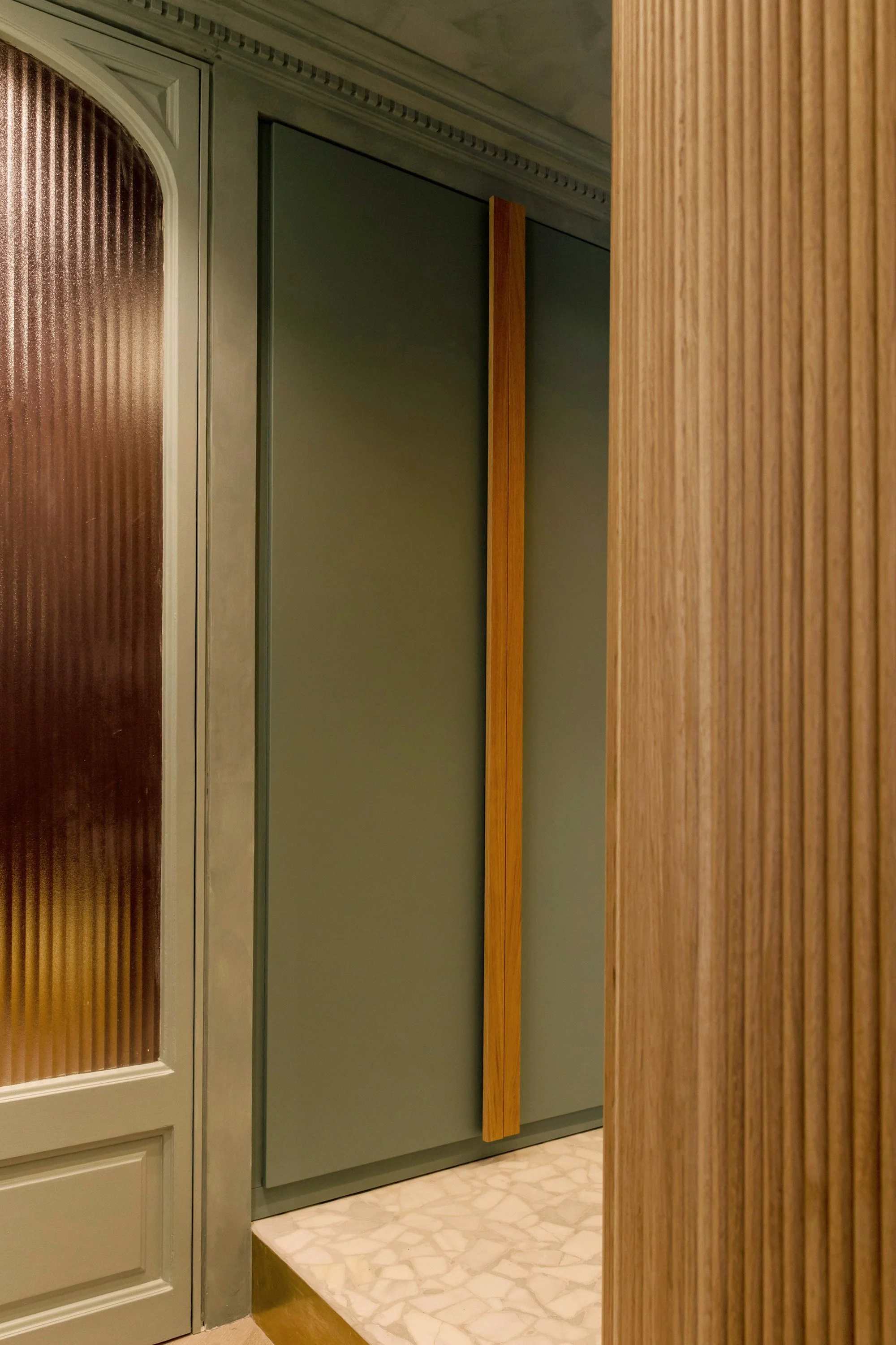 Close-up of olive green sliding door with a vertical wooden handle, adjacent to a textured glass door and wooden wall panels.