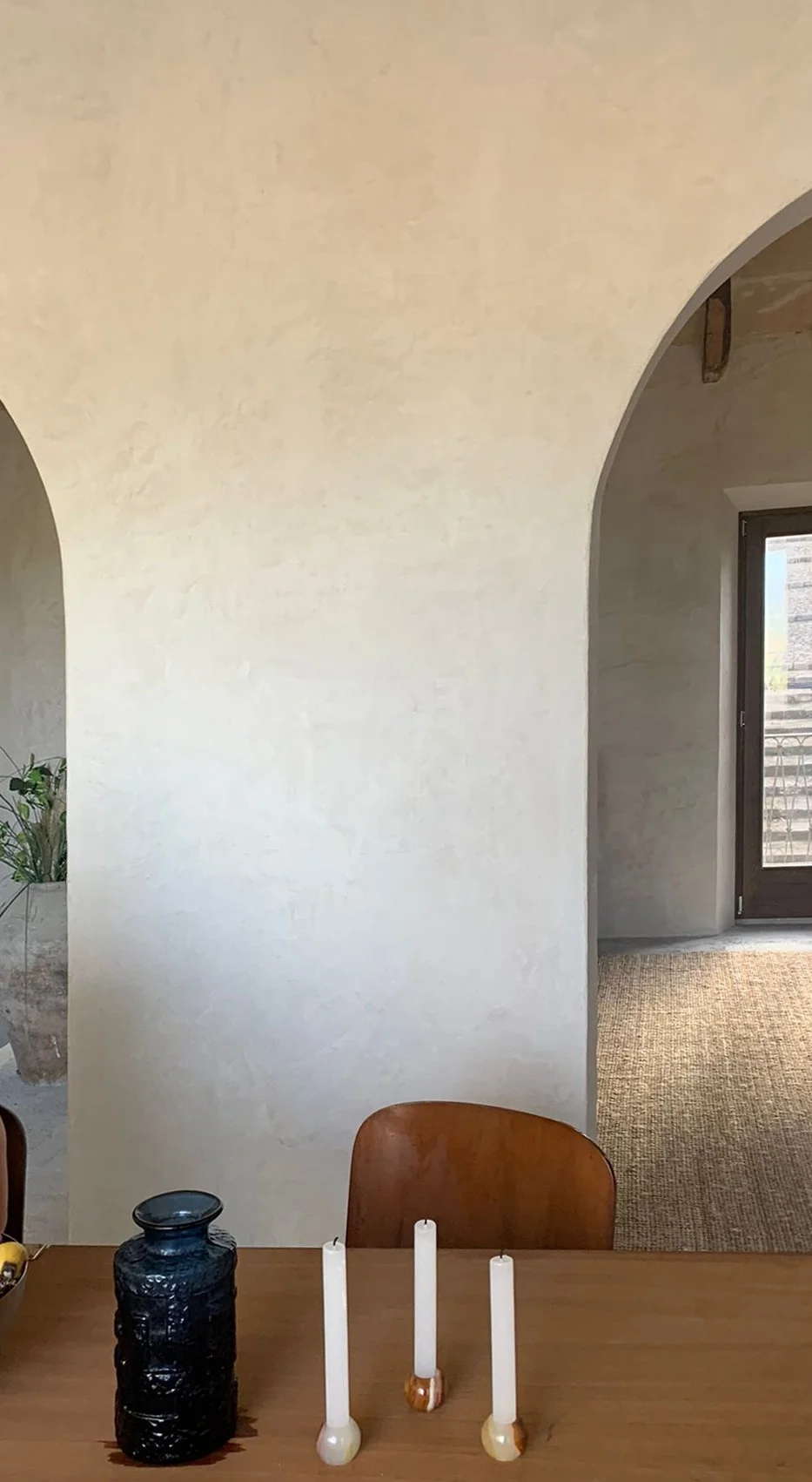  Interior view of a room with a curved arched wall, a table with candles and a vase, and a door with glass window leading outside.