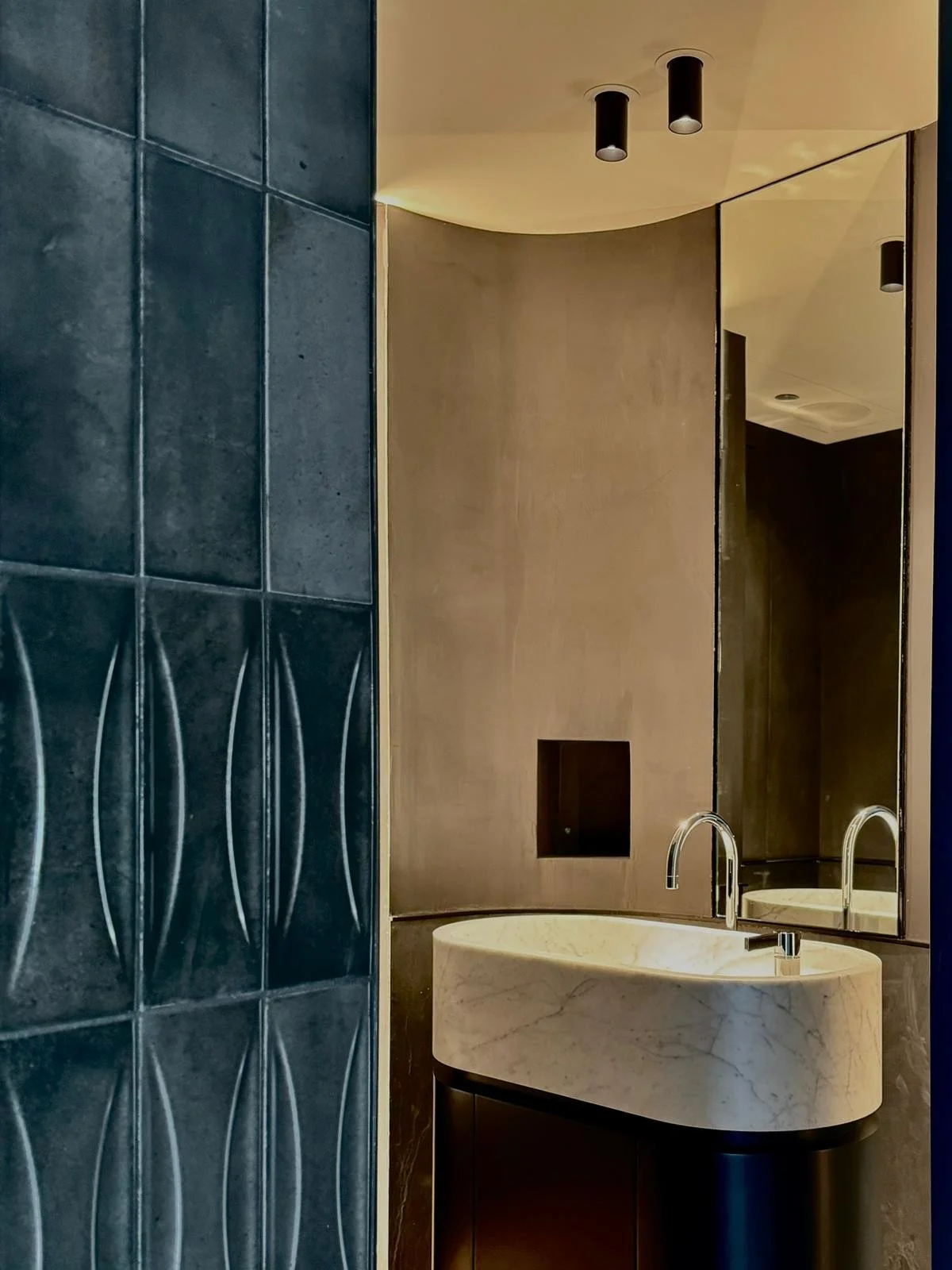 A modern bathroom featuring a large mirror, a marble vessel sink, and dark decorative tiles.