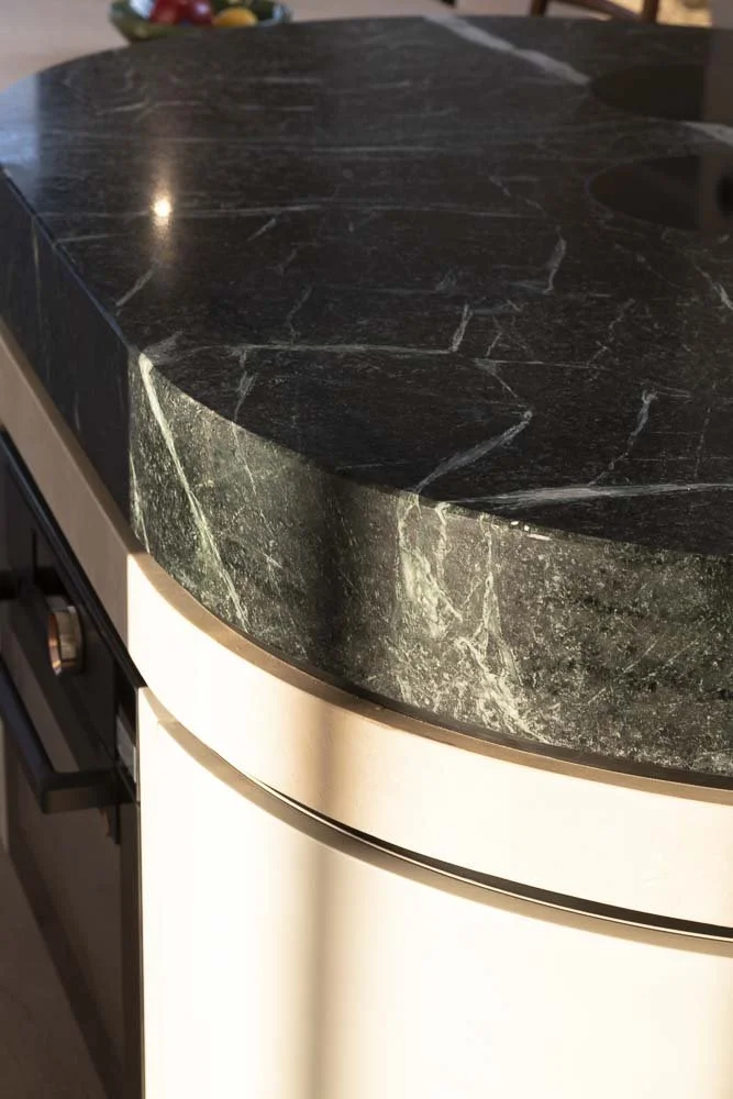 Close-up of a dark green marble kitchen countertop with white veins over a beige cabinet.