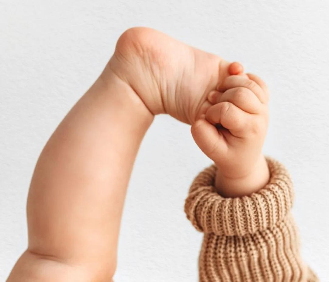 Close-up of a child's hand clenched into a fist, with the arm wearing a beige knit sweater. The background is plain white.
