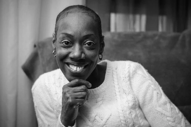 Black woman smiling and resting her chin on her hand in black and white