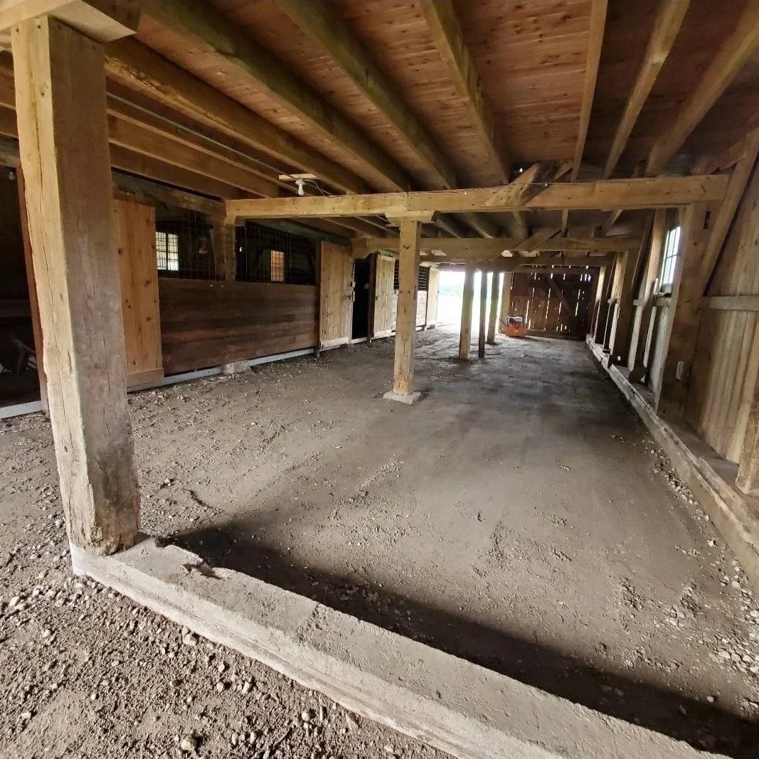 Interior of a barn under construction with wooden beams, dirt floor, and partially enclosed sections.