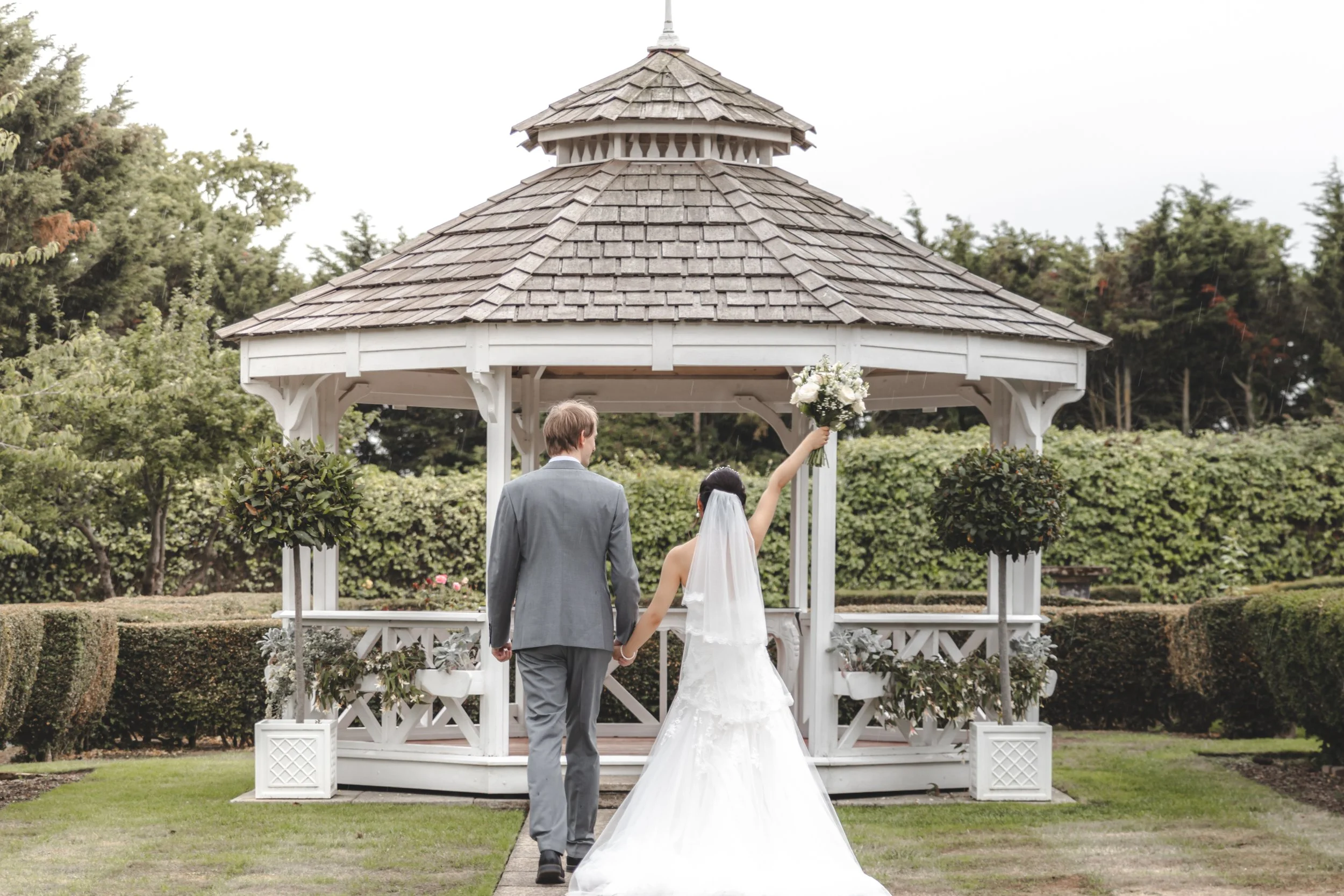Bride and groom walking hand in hand towards a bandstand during their Dorset wedding, with the bride holding her bouquet, captured naturally and candidly.