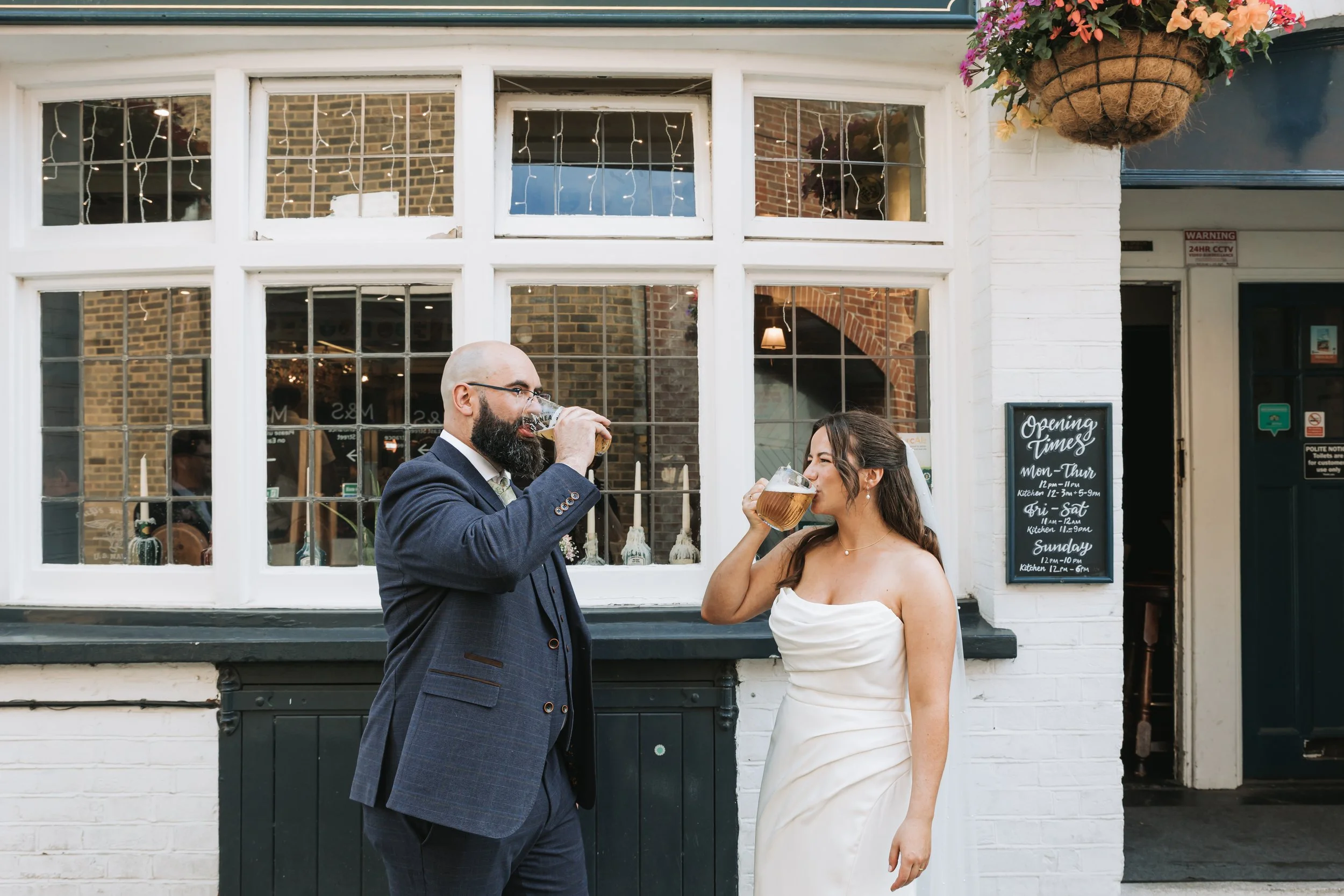 Bride and groom on their wedding day drinking pints outside the Hole in the Wall pub in Chichester.
