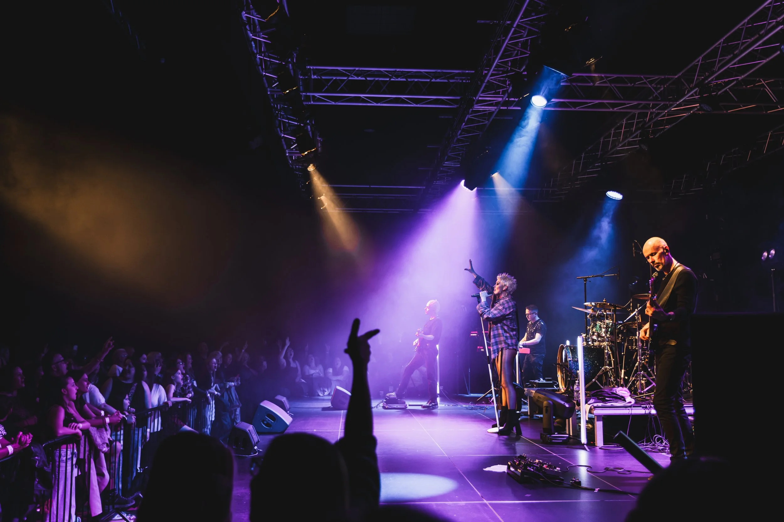 Live music concert with a band performing on stage under colorful lighting with an enthusiastic audience in front.