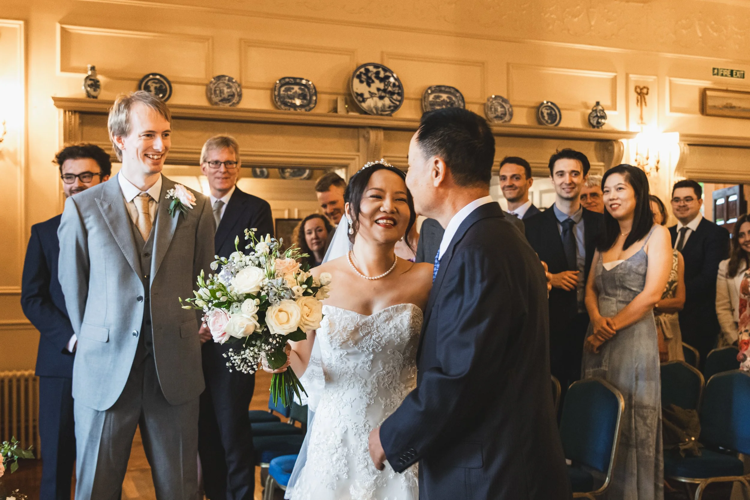 Bride walking down the aisle with her father giving her away, while the groom smiles, captured during a Dorset wedding in a natural, emotional moment.