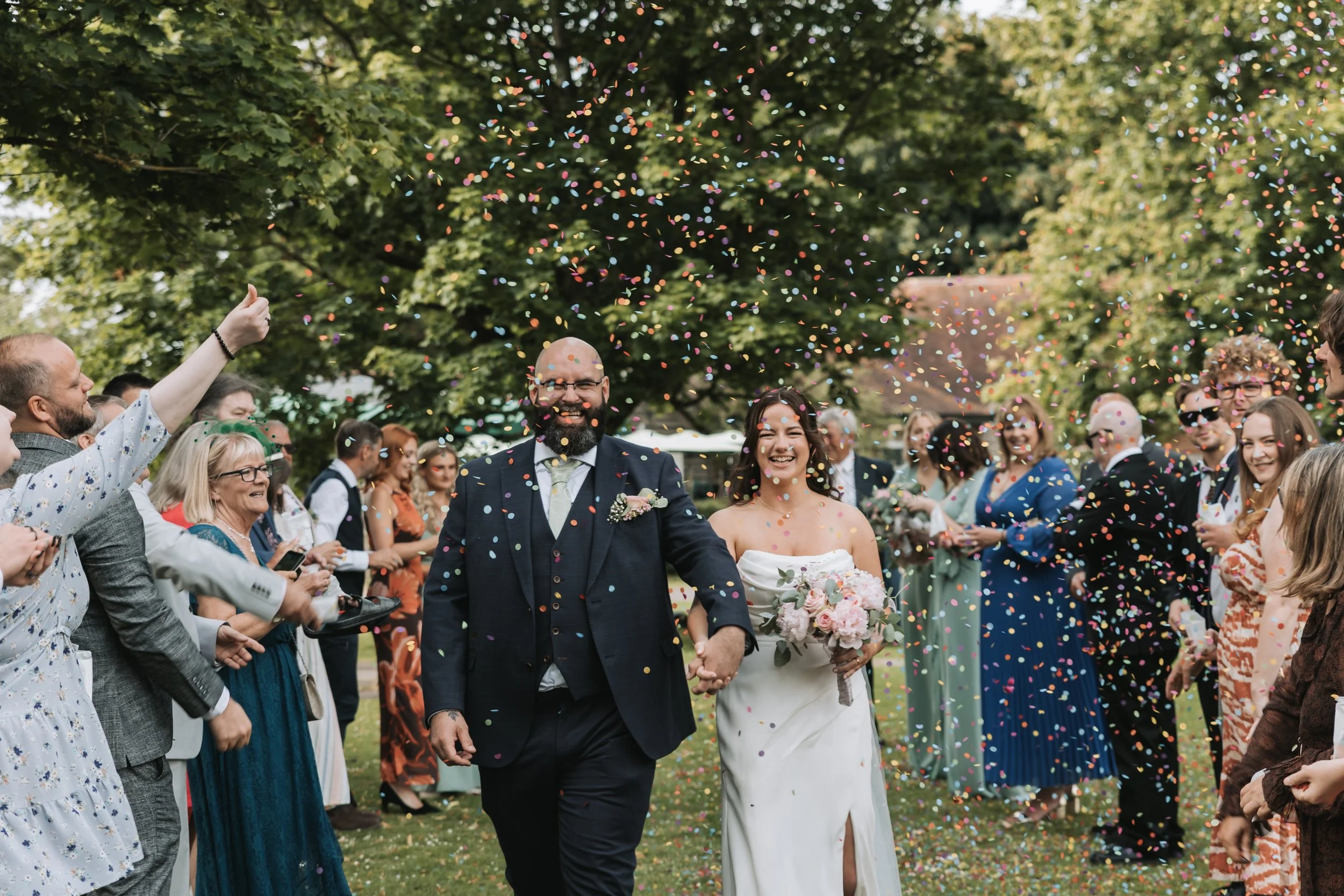 A newlywed couple walking with confetti in Priory Park, Chichester.