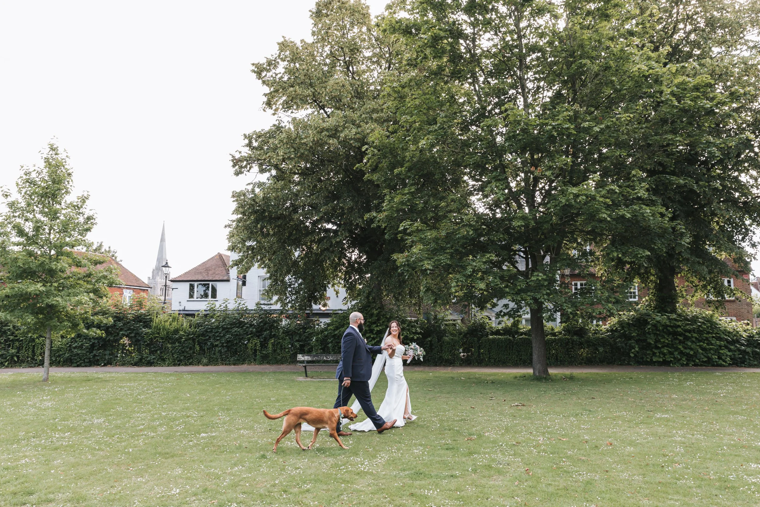 Bride and groom walk their dog on their wedding day in Priory Park in Chichester.