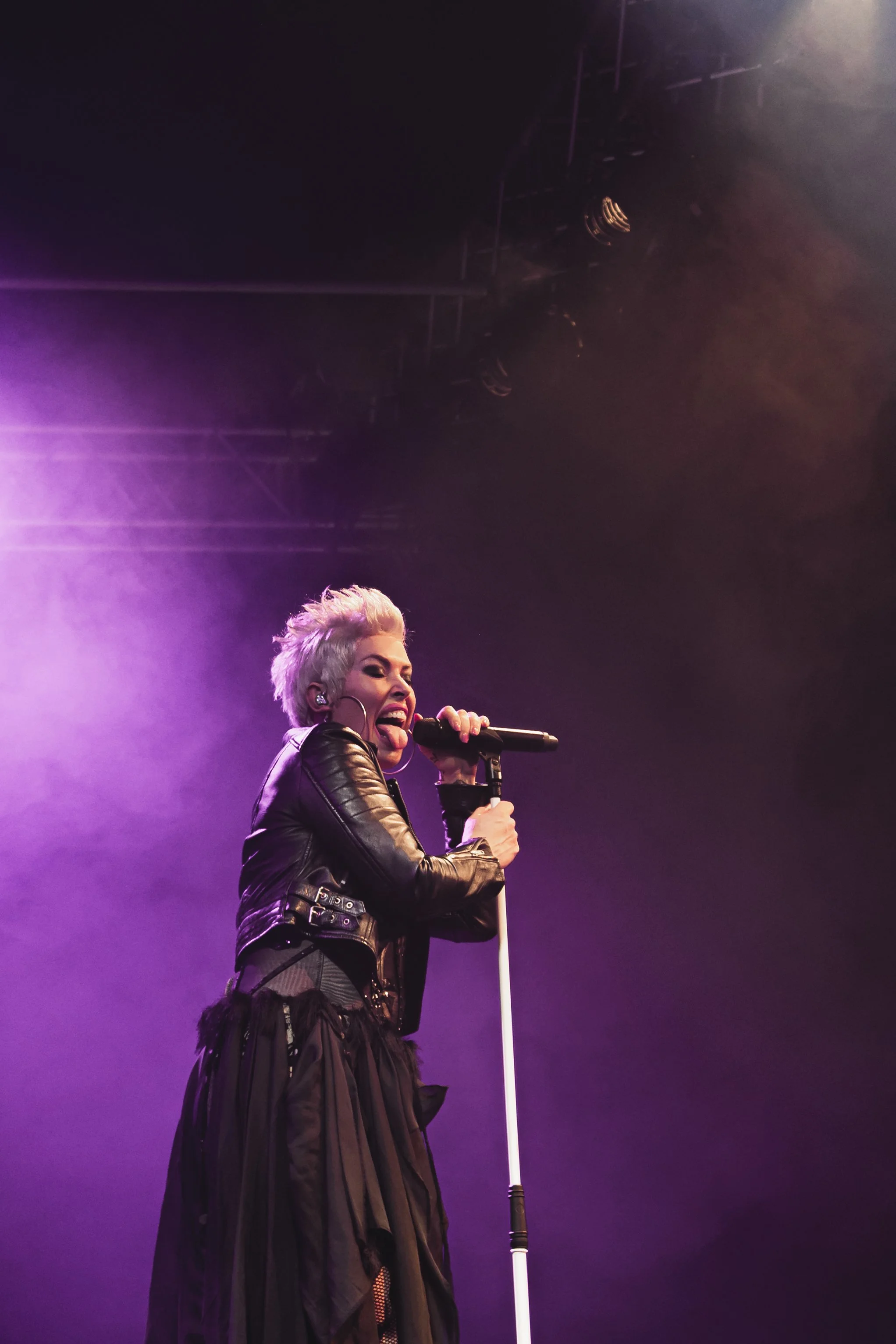 A woman with platinum blonde hair singing into a microphone on stage with purple lighting.