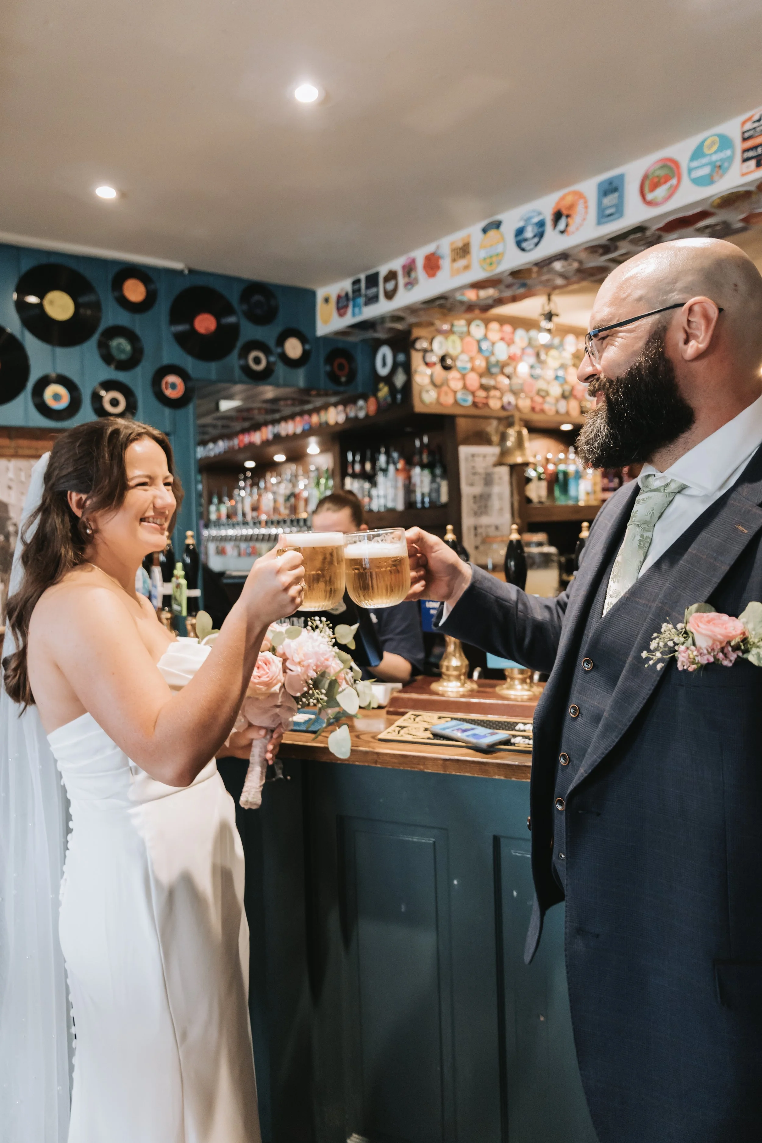 Bride and groom cheers with beers inside Hole in the Wall pub in Chichester.
