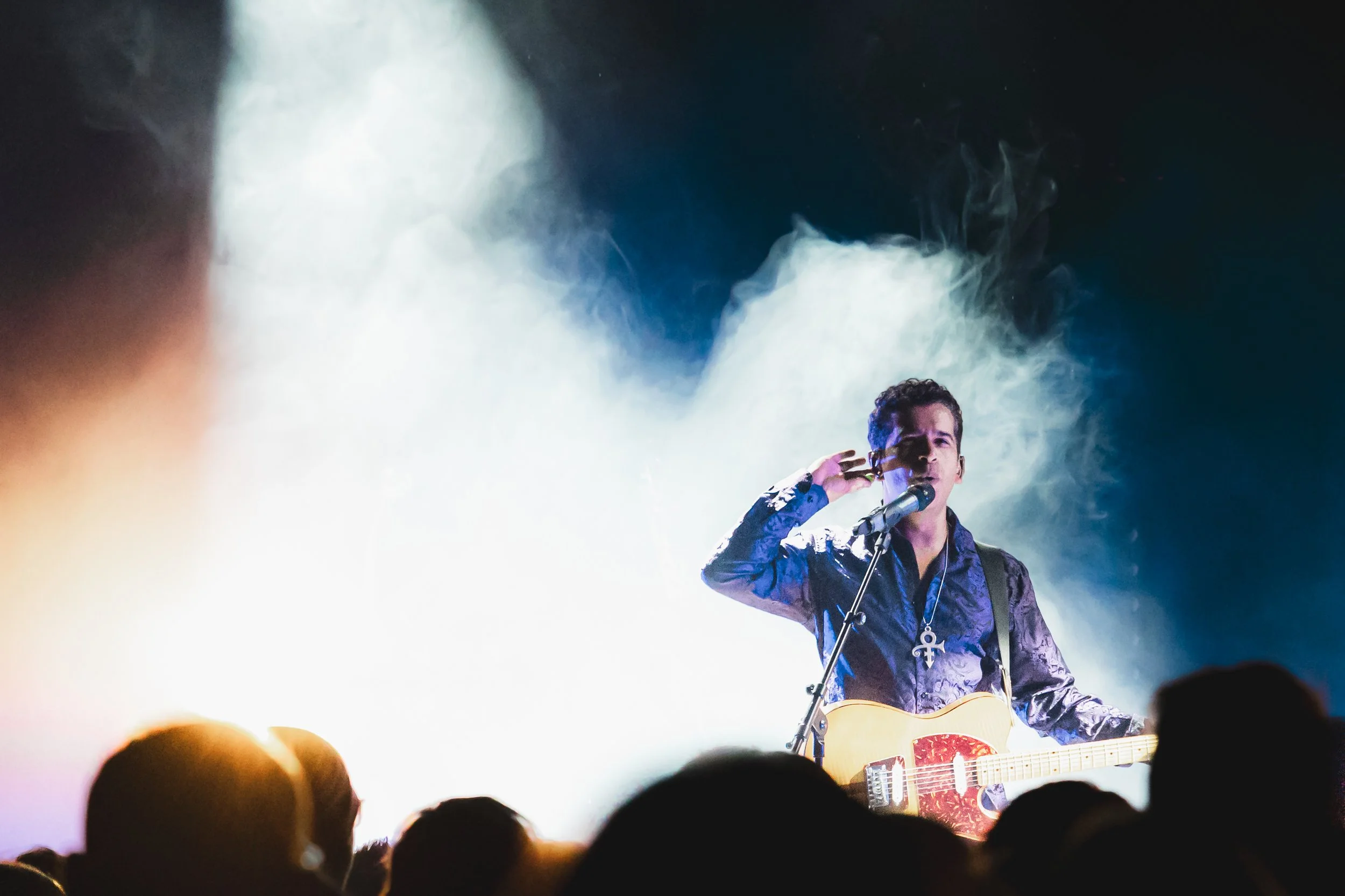 Prince tribute act, New Purple Celebration performing on stage with a guitar, in front of an audience, with dramatic lighting and smoky effects.