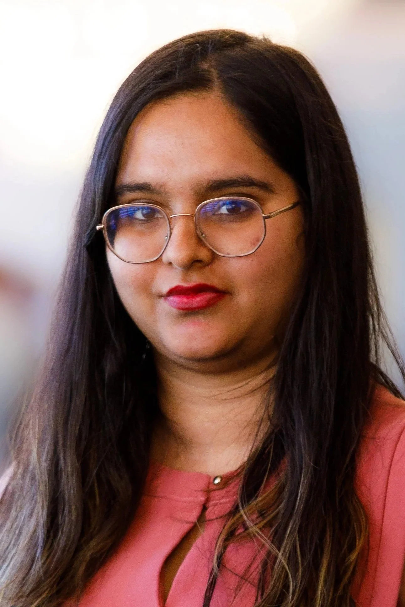 A young woman with long dark hair, glasses, and red lipstick wearing a pink top.