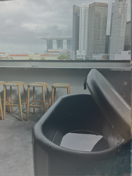 Indoor lounge with black chair and three wooden stools in front of a window overlooking a city skyline with tall office buildings and the Marina Bay Sands hotel in Singapore.