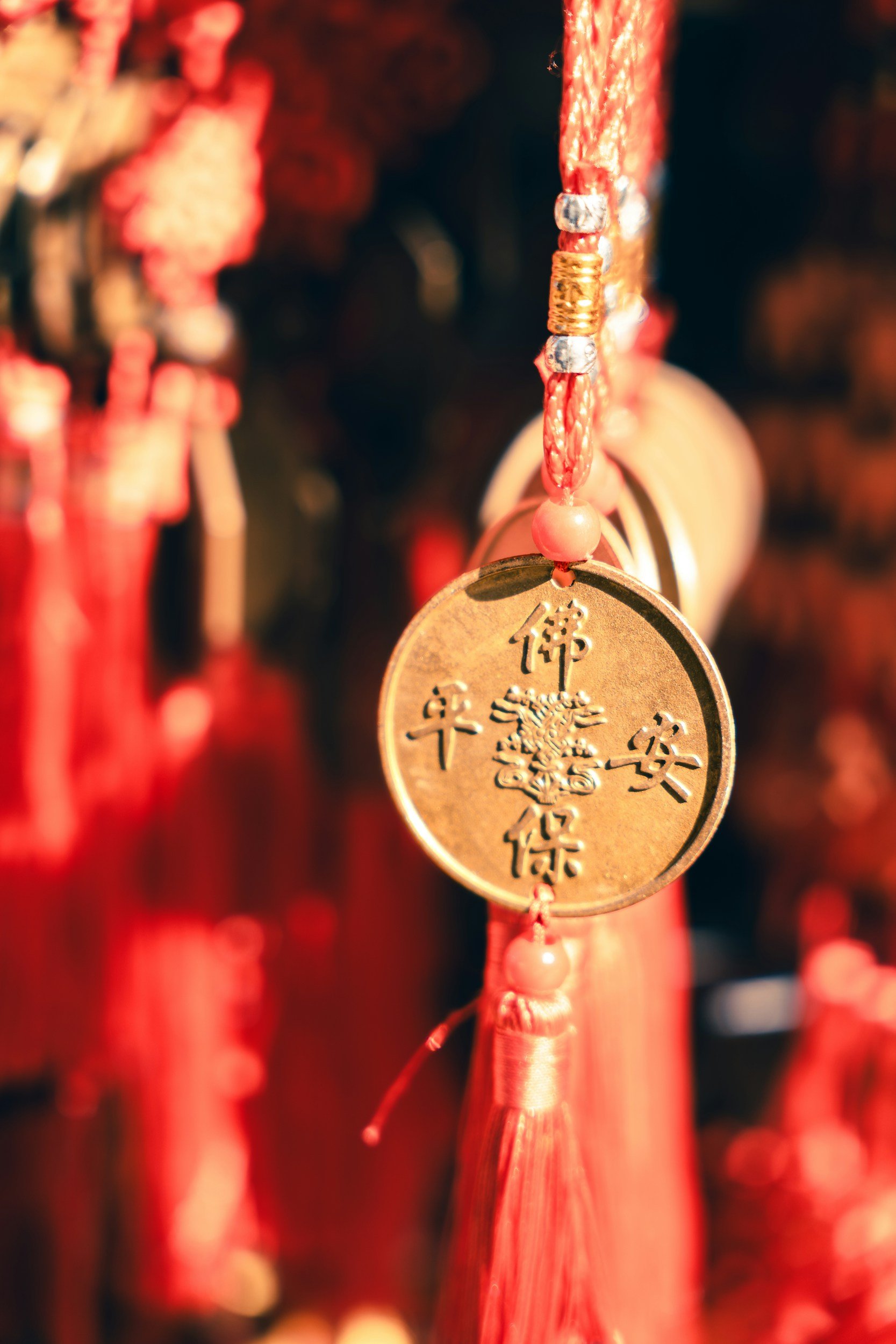 Gold medallion with Chinese characters hanging from a red string with beads and tassel, likely part of traditional Chinese decorations.