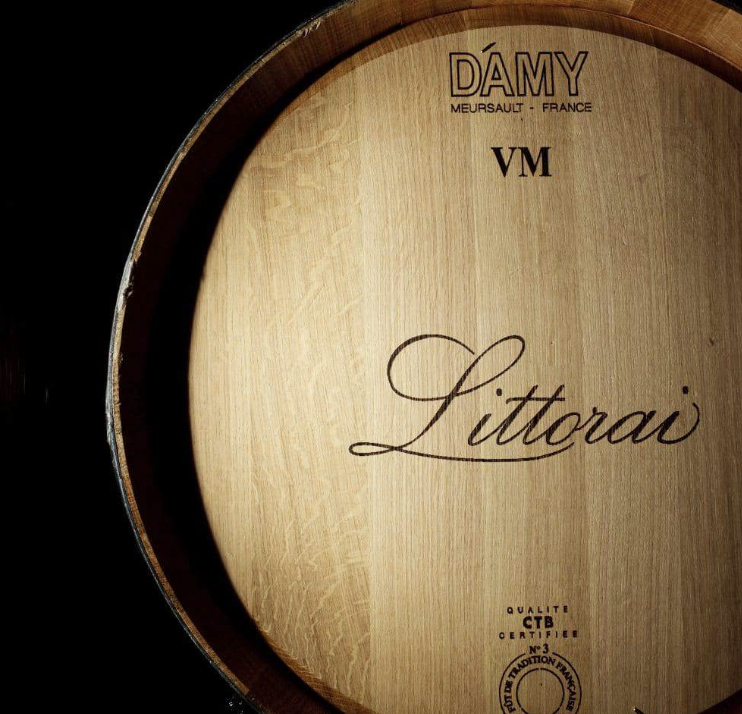 Close-up of a wooden wine barrel with the brand name 'DÁMY', location 'Meursault, France', and the wine name 'Littoral' engraved on it.