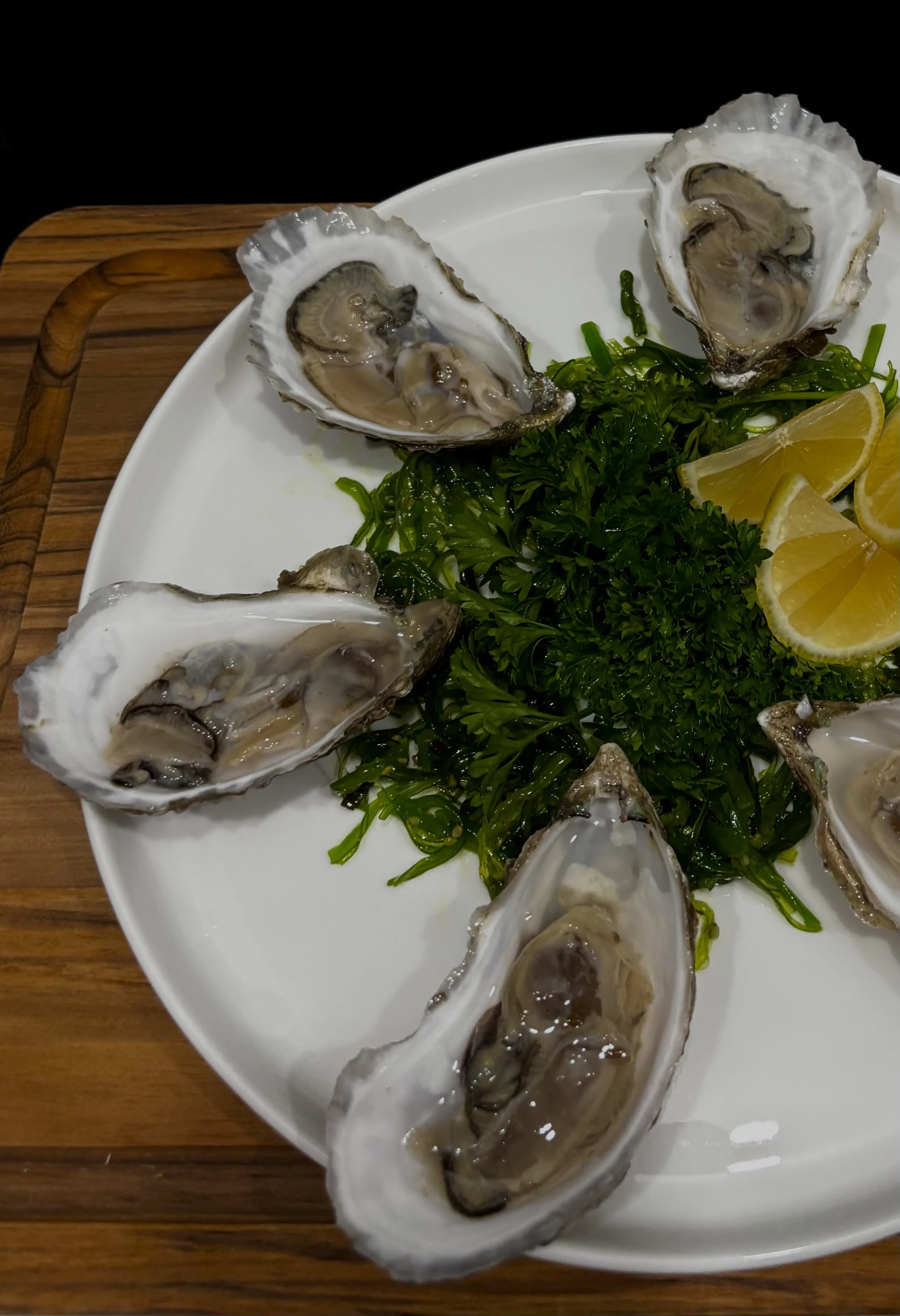 A plate of fresh oysters on a bed of green garnish with lemon wedges Private chef dallas