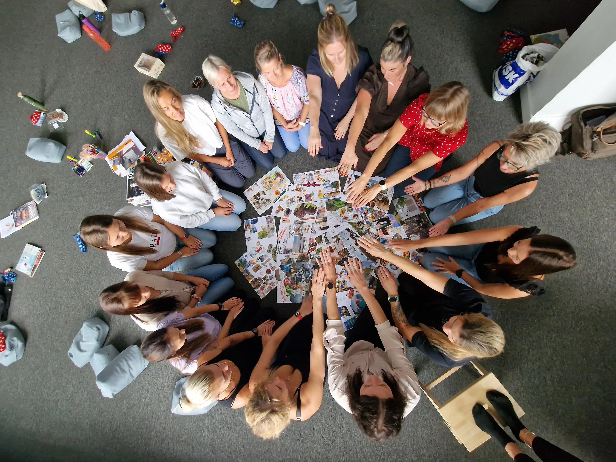 Group of women sitting and standing around a circle of magazines on the floor, engaging in a discussion or activity.