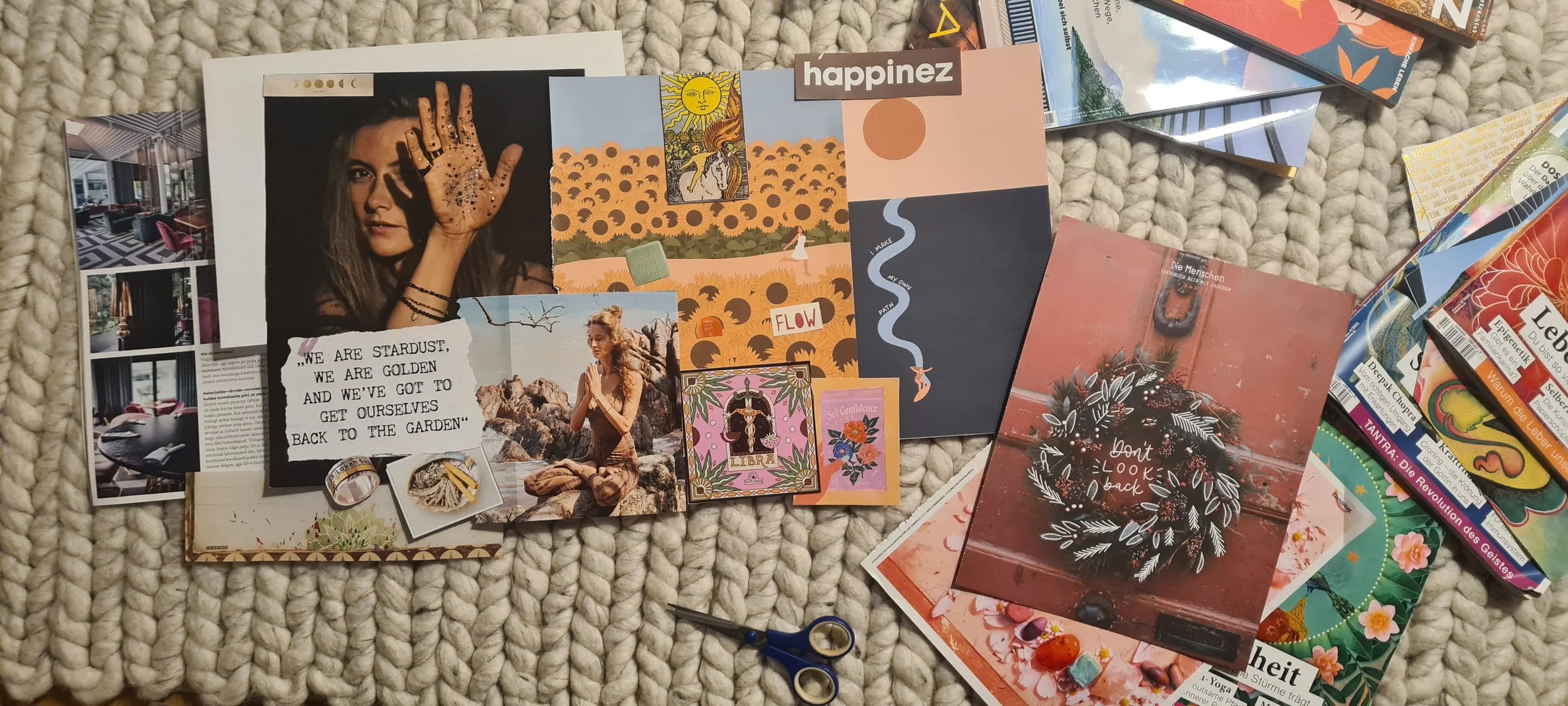 A flat lay of various colorful postcards, photographs, and small art prints spread on a textured beige rug. Items include a photo of a woman with henna on her hand, a picture of a woman meditating by rocks, several artistic designs with nature themes