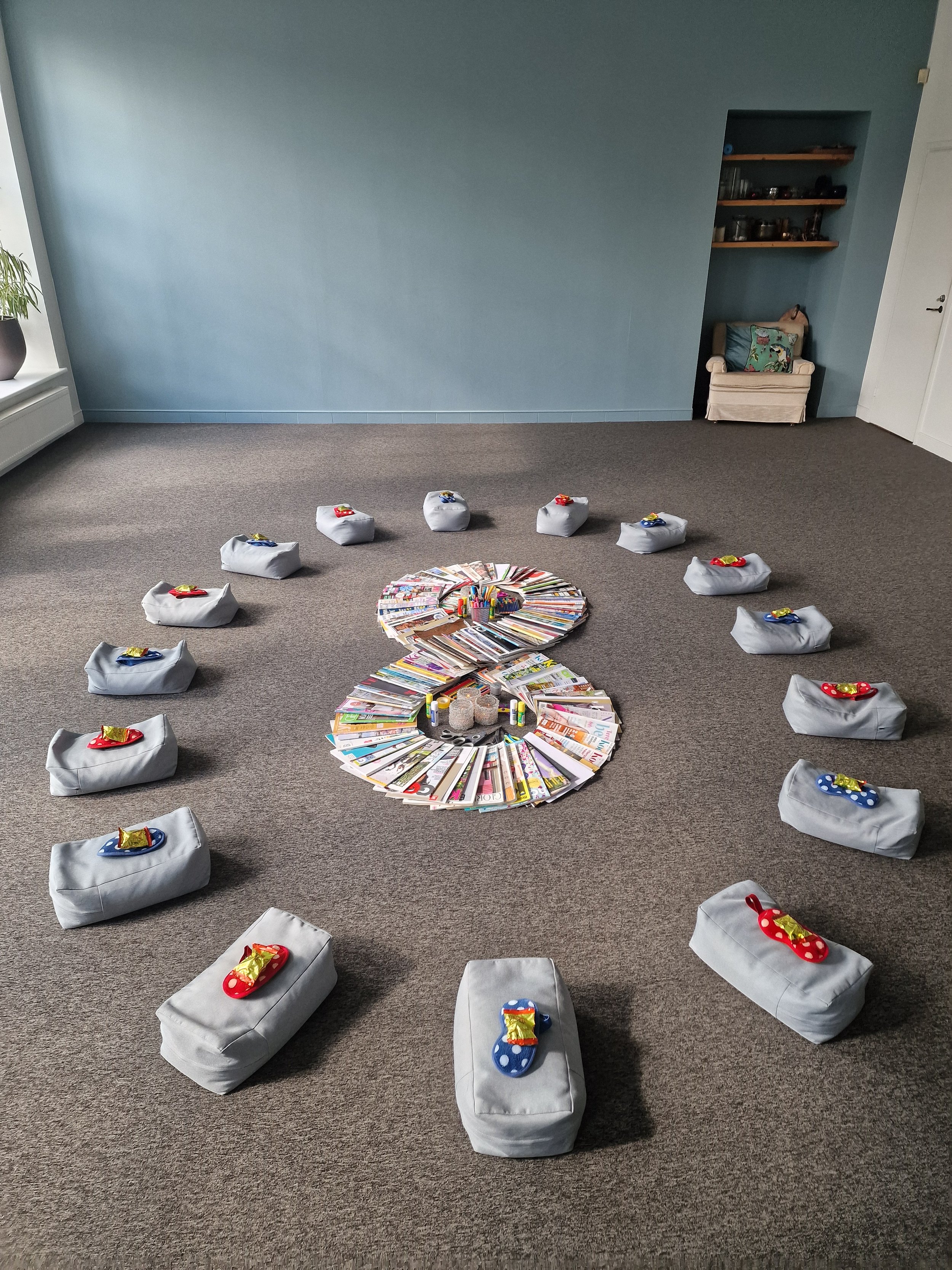 Indoor room with a gray carpet and green wall, decorated with a large number 8 made from magazines, surrounded by gray pillows with colorful small wrapped gifts on top.