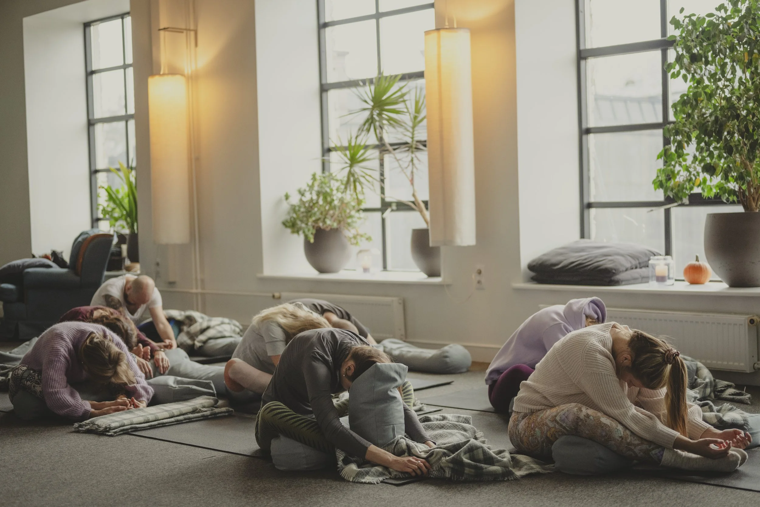 Group of people practicing yoga in a spacious, well-lit room with large windows and indoor plants.