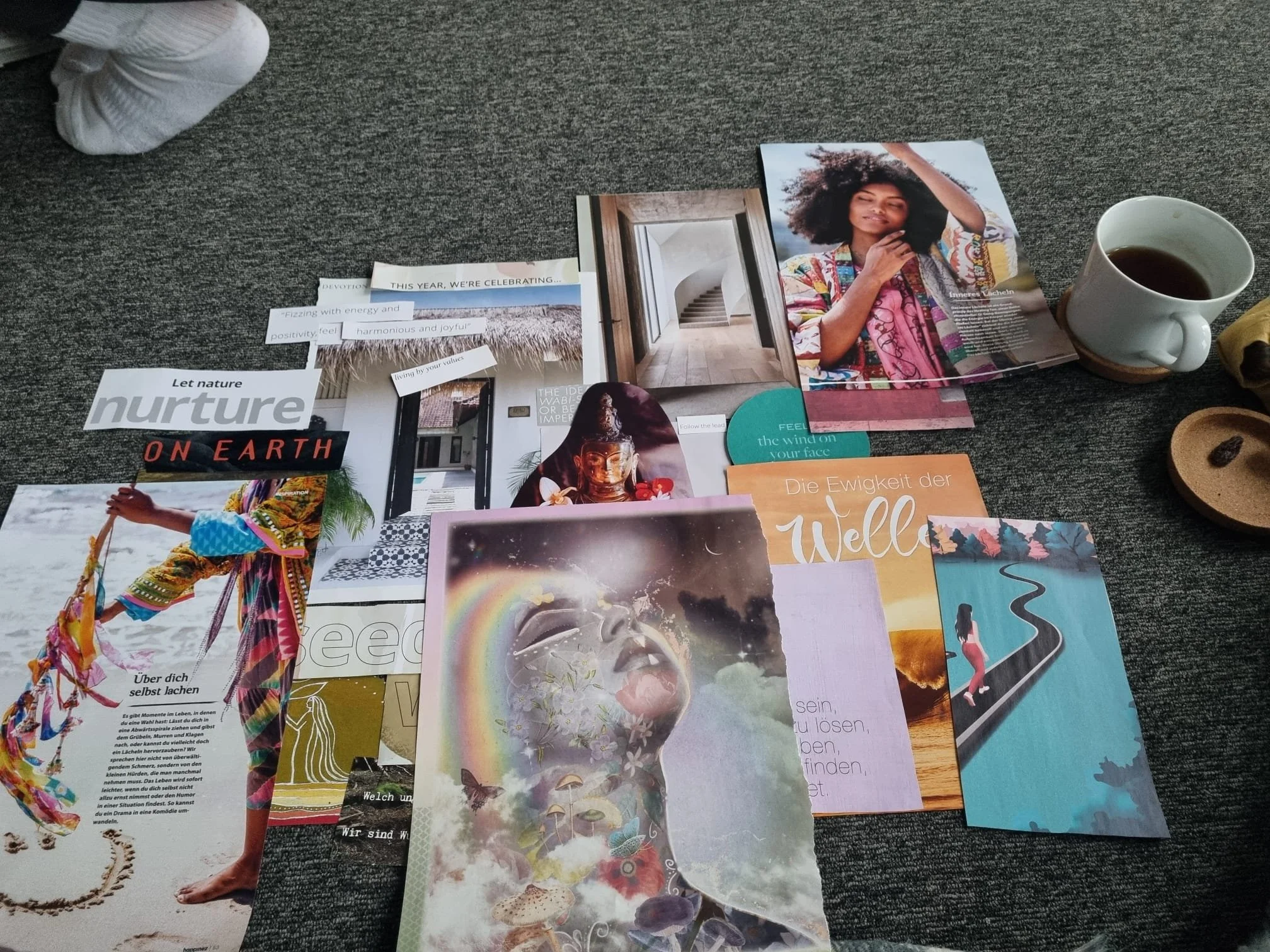 A collection of assorted magazines, photographs, and paper cutouts spread out on a gray carpeted floor, including an image of a woman with curly hair, a cup of coffee, and various colorful posters and articles.