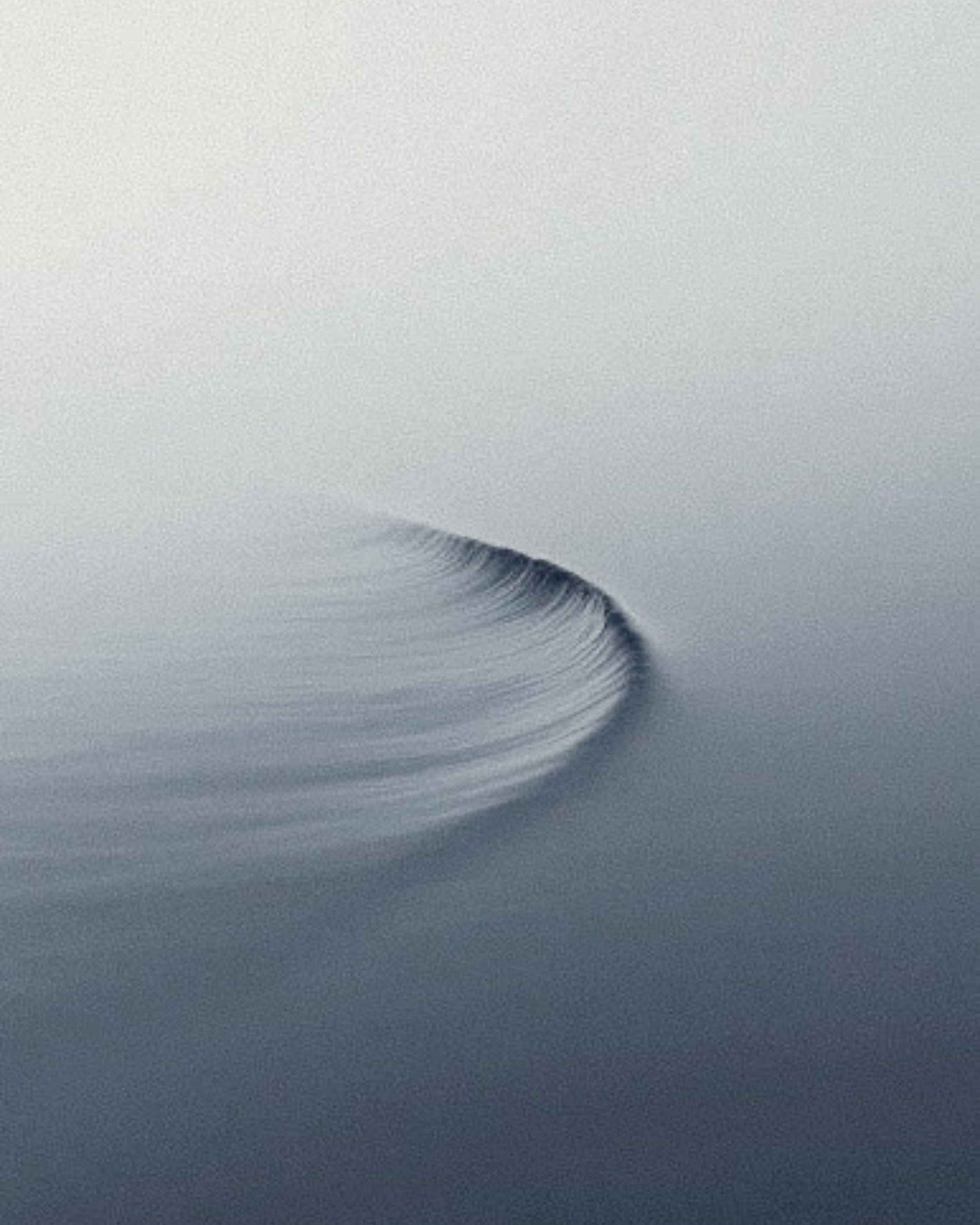 A minimalist photograph showing a small section of ripples on a calm body of water, with a gentle wave or curved ripple near the center.