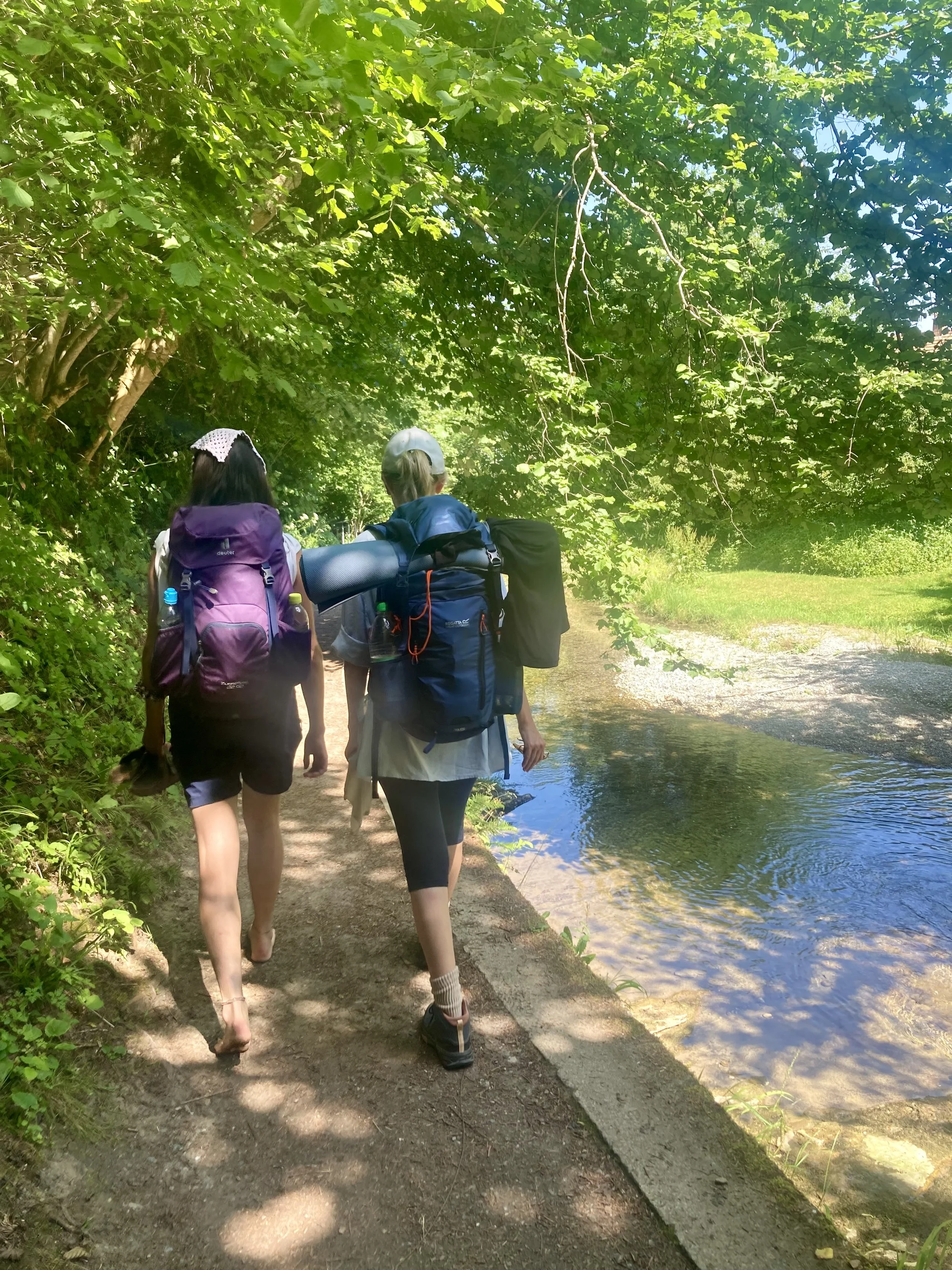zwei Pilgerinnen mit Rucksack entlang eines Flusses im Wald. Systemische Therapie und Beratung in Landshut