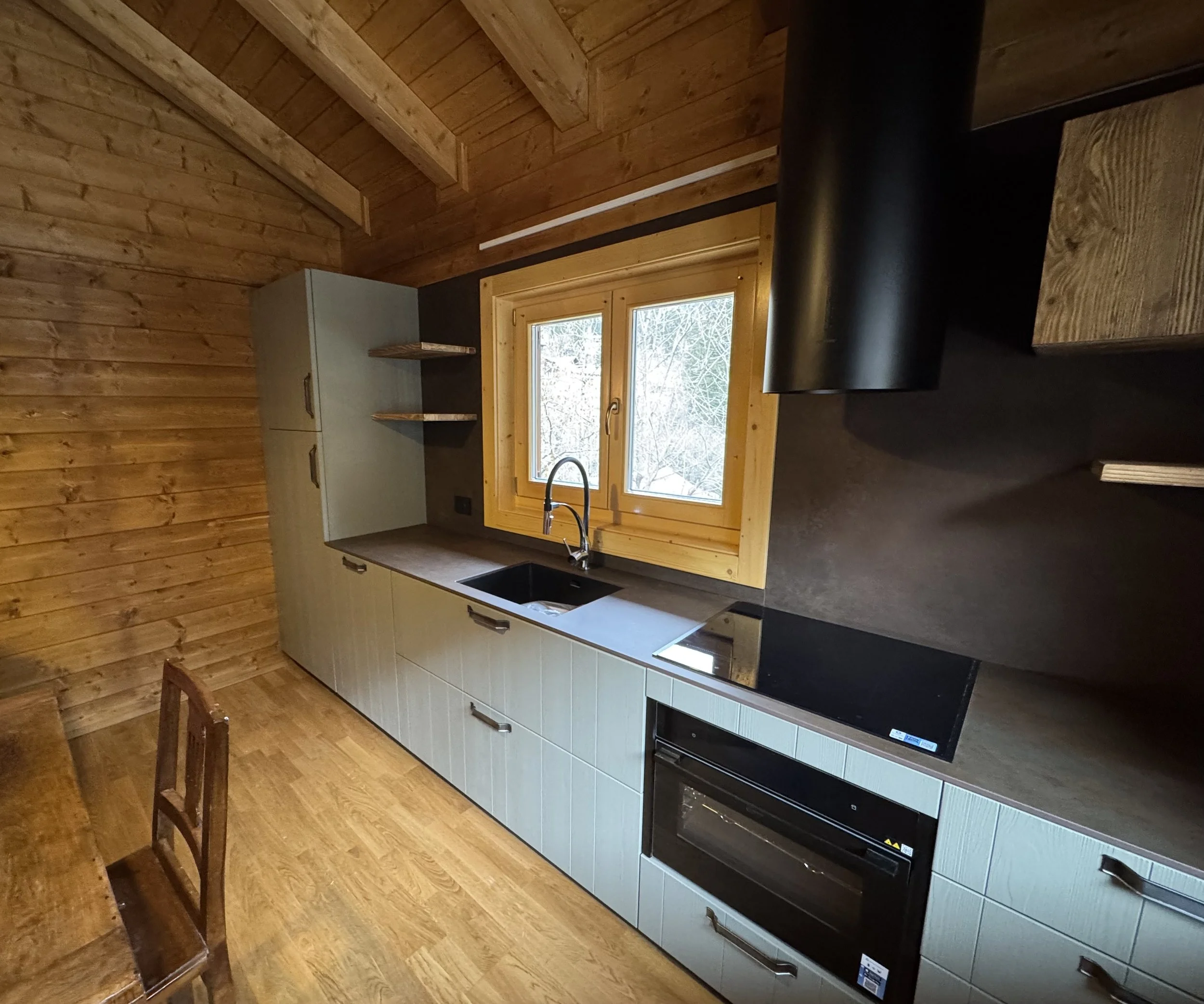 Cucina in stile rustico con mobili chiari, pannelli di legno e una finestra con vista sul paesaggio invernale