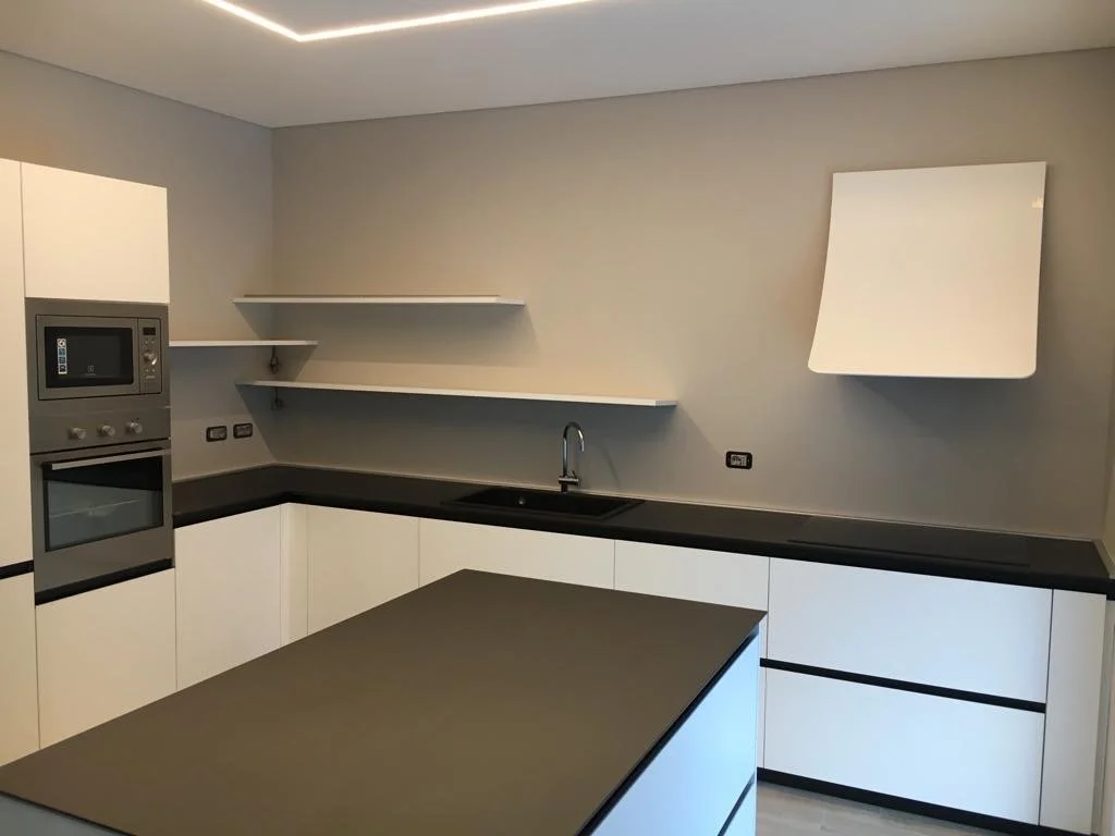 Cucina moderna con armadietti bianchi, piano di lavoro nero, forno, microonde, lavello e mensole sulla parete di sfondo.