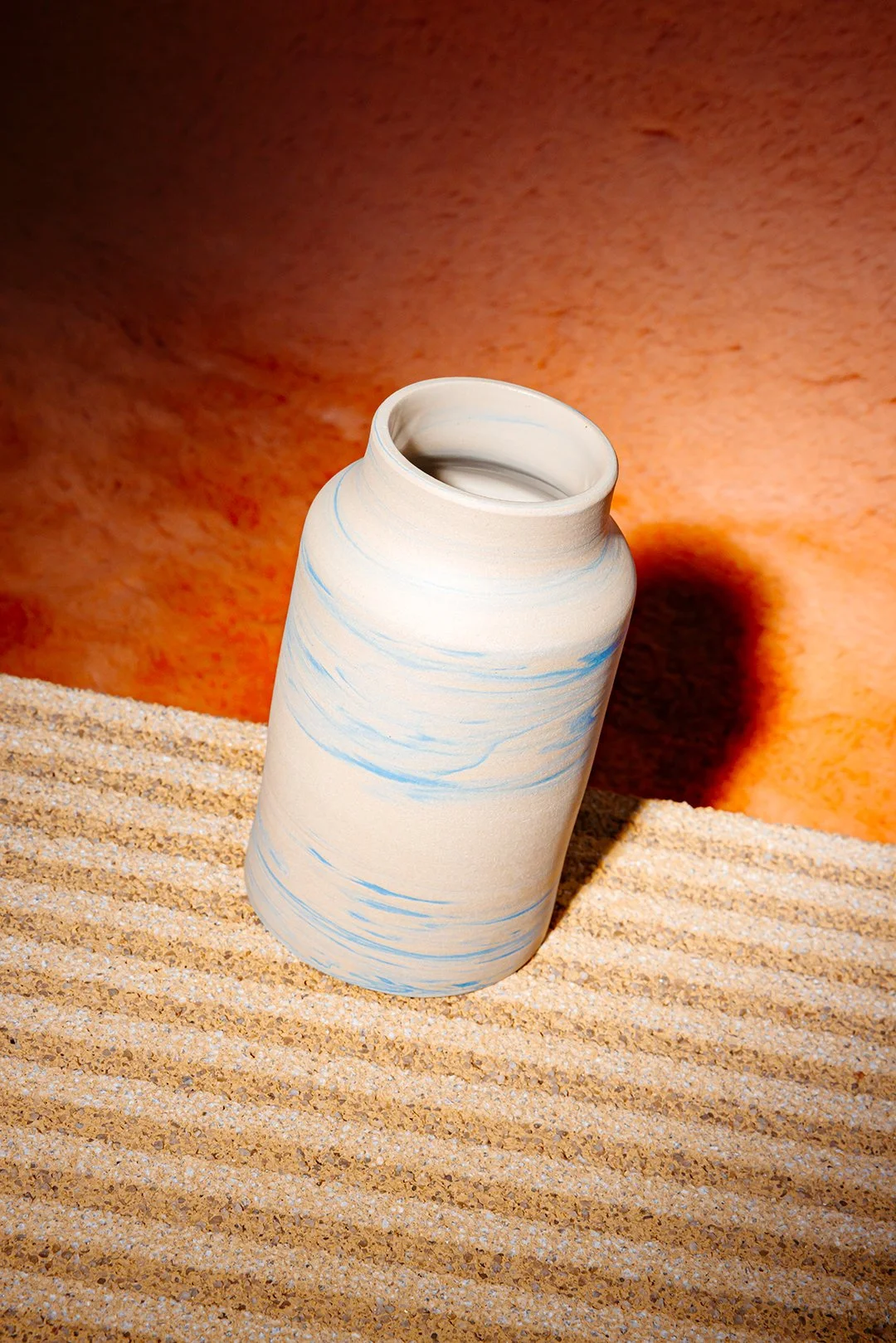 Keramikvase mit blauen Strichen auf Sand und einem orangefarbenen Hintergrund.