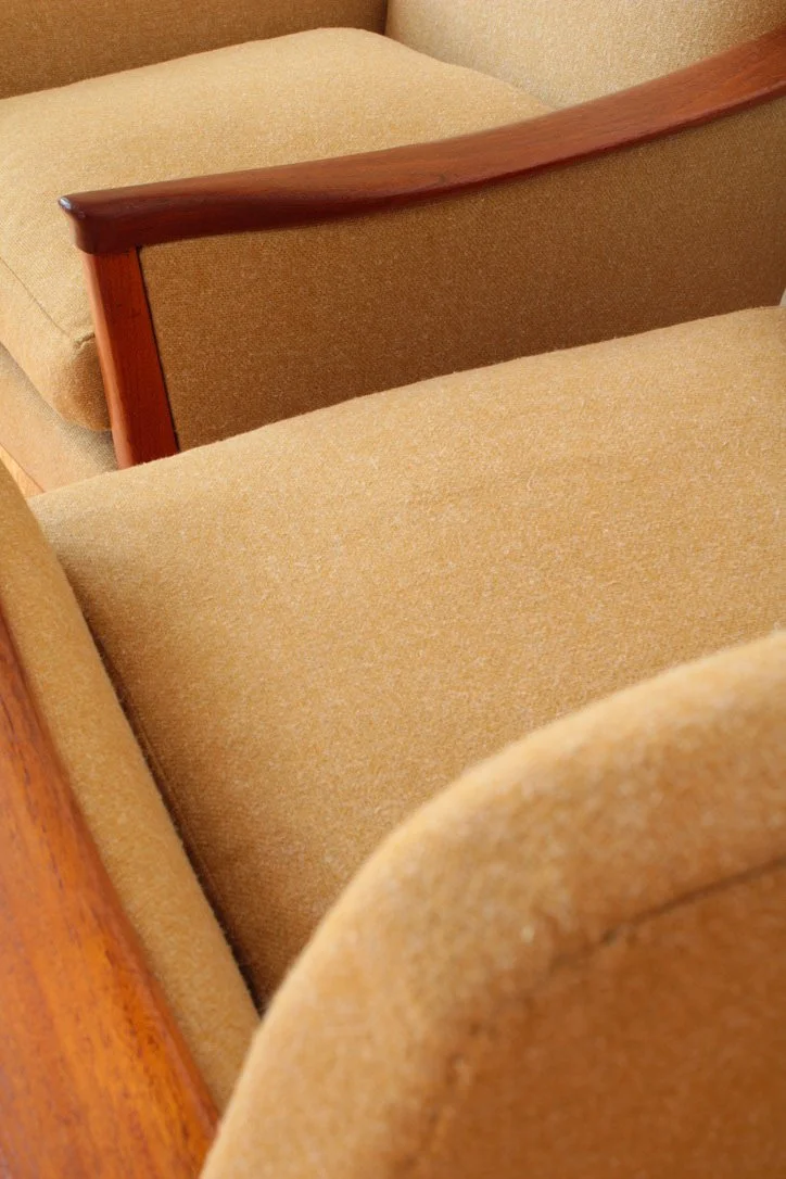 Close-up of upholstered beige armchairs with wooden armrests in a waiting room or auditorium.