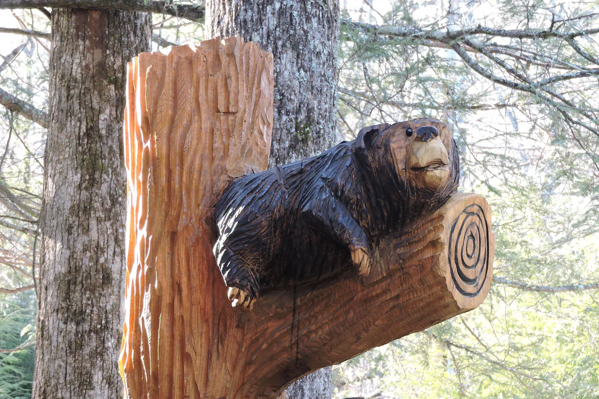 Wooden carved bear sculpture on a tree trunk in a forest.