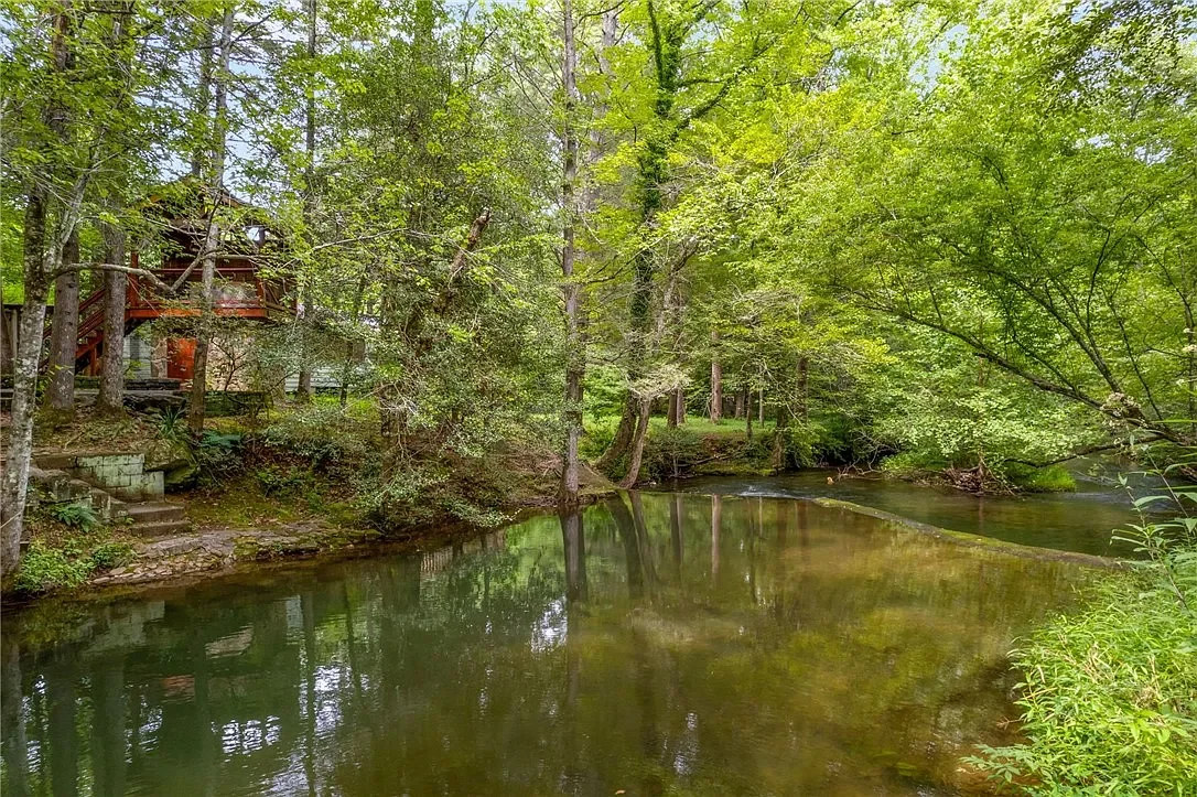 A wooden deck with stairs leading down to a river, surrounded by lush green trees in a forest setting.