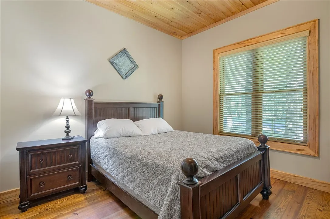 A bedroom with a dark wooden bed frame, a nightstand with a lamp, and a window with wooden blinds and frame.